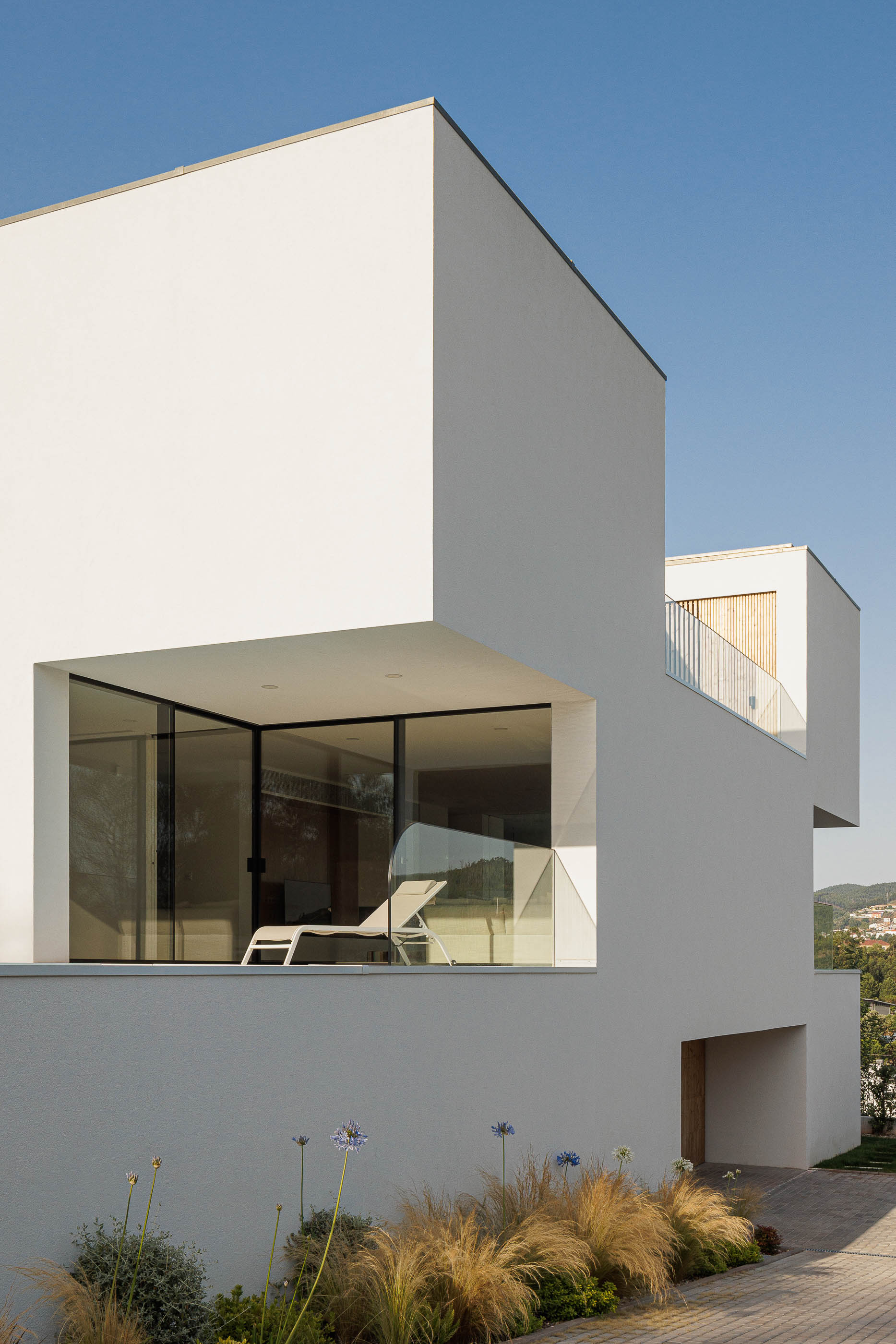 Exterior da casa com arquitetura moderna e minimalista. Volumes brancos e jardim com vegetação. — Casa JC arquitetura Mário Alves Arquitecto em Coimbra
