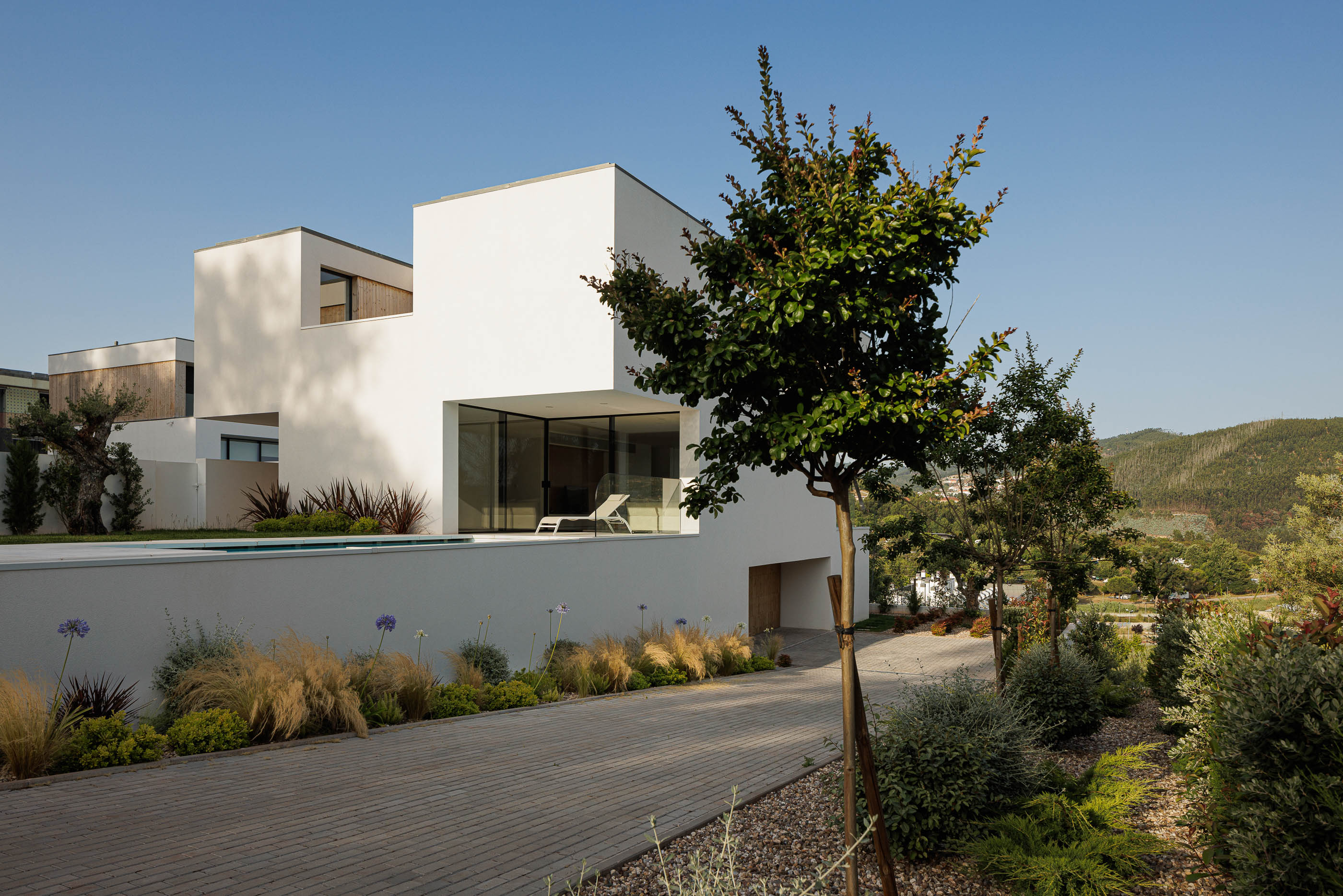 Exterior da casa ao entardecer com iluminação. Arquitetura moderna com volumes brancos e jardim. — Casa JC arquitetura Mário Alves Arquitecto em Coimbra