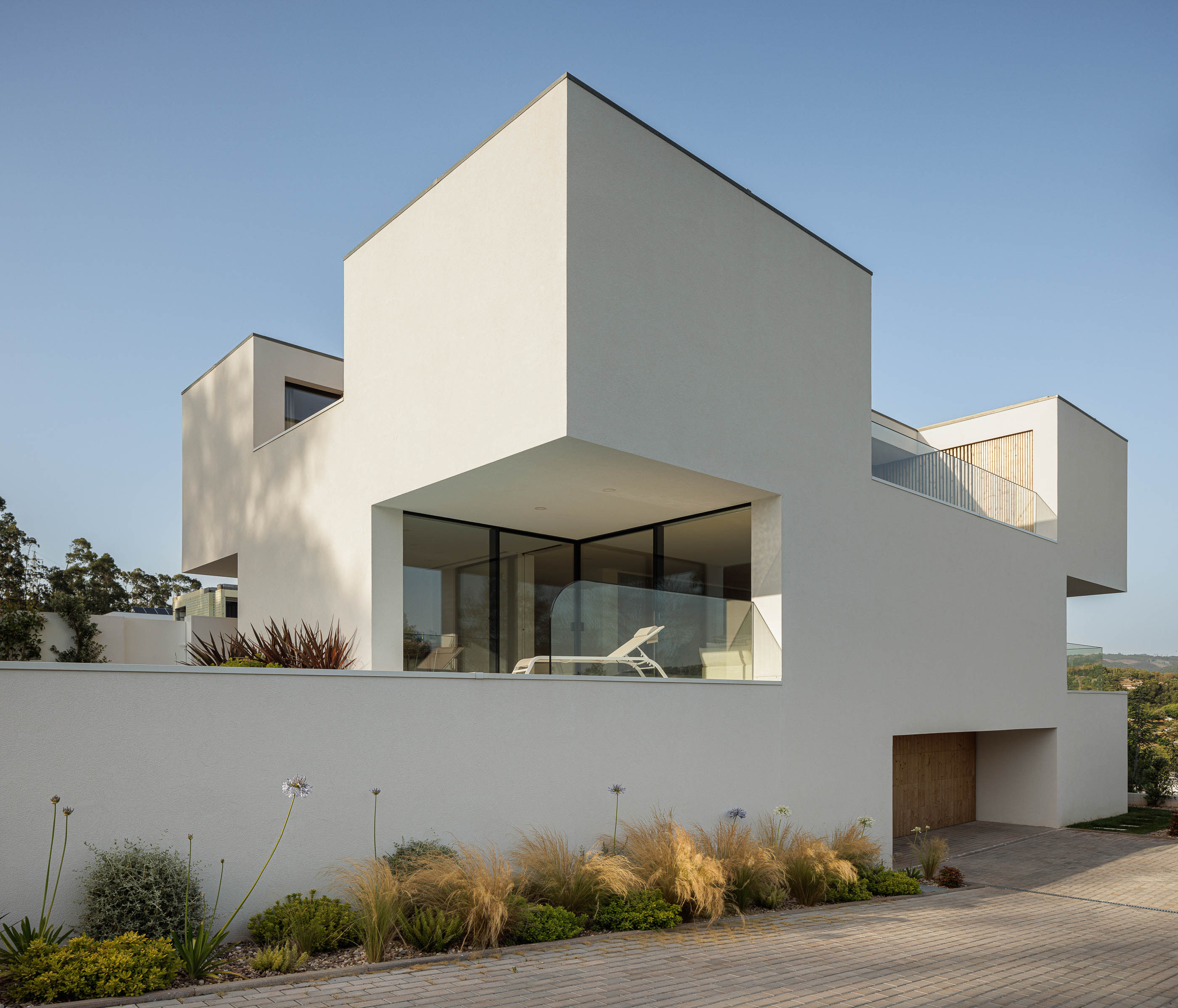 Fachada da casa ao entardecer com porta em madeira. Arquitetura moderna com volumes brancos. — Casa JC arquitetura Mário Alves Arquitecto em Coimbra
