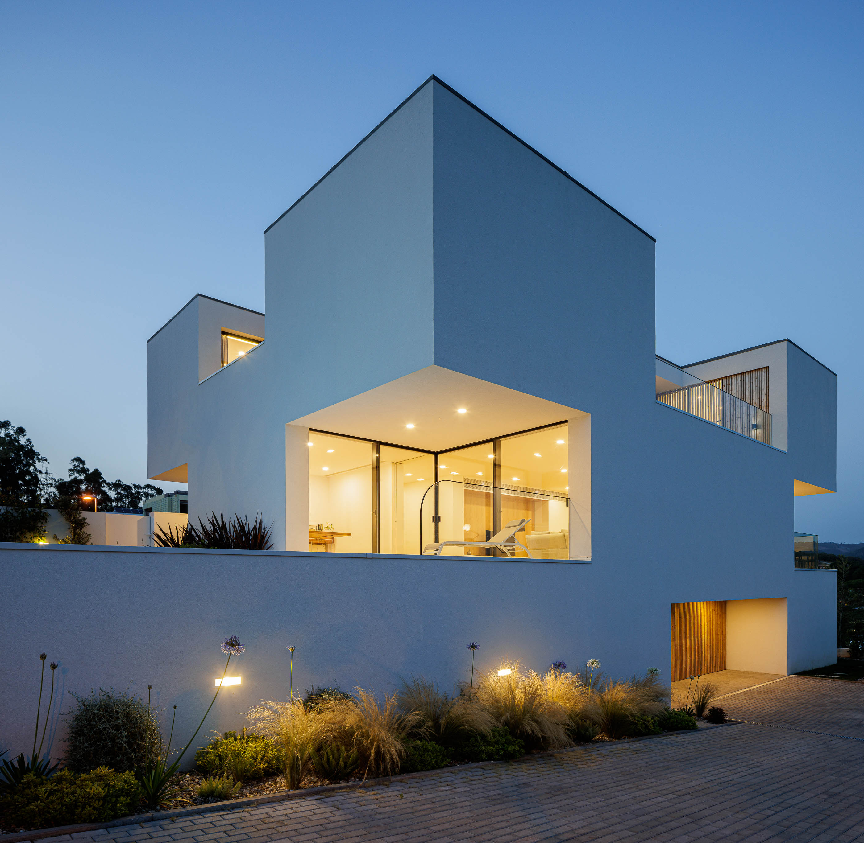 Exterior da casa ao anoitecer com iluminação. Arquitetura moderna com volumes brancos e jardim. — Casa JC arquitetura Mário Alves Arquitecto em Coimbra