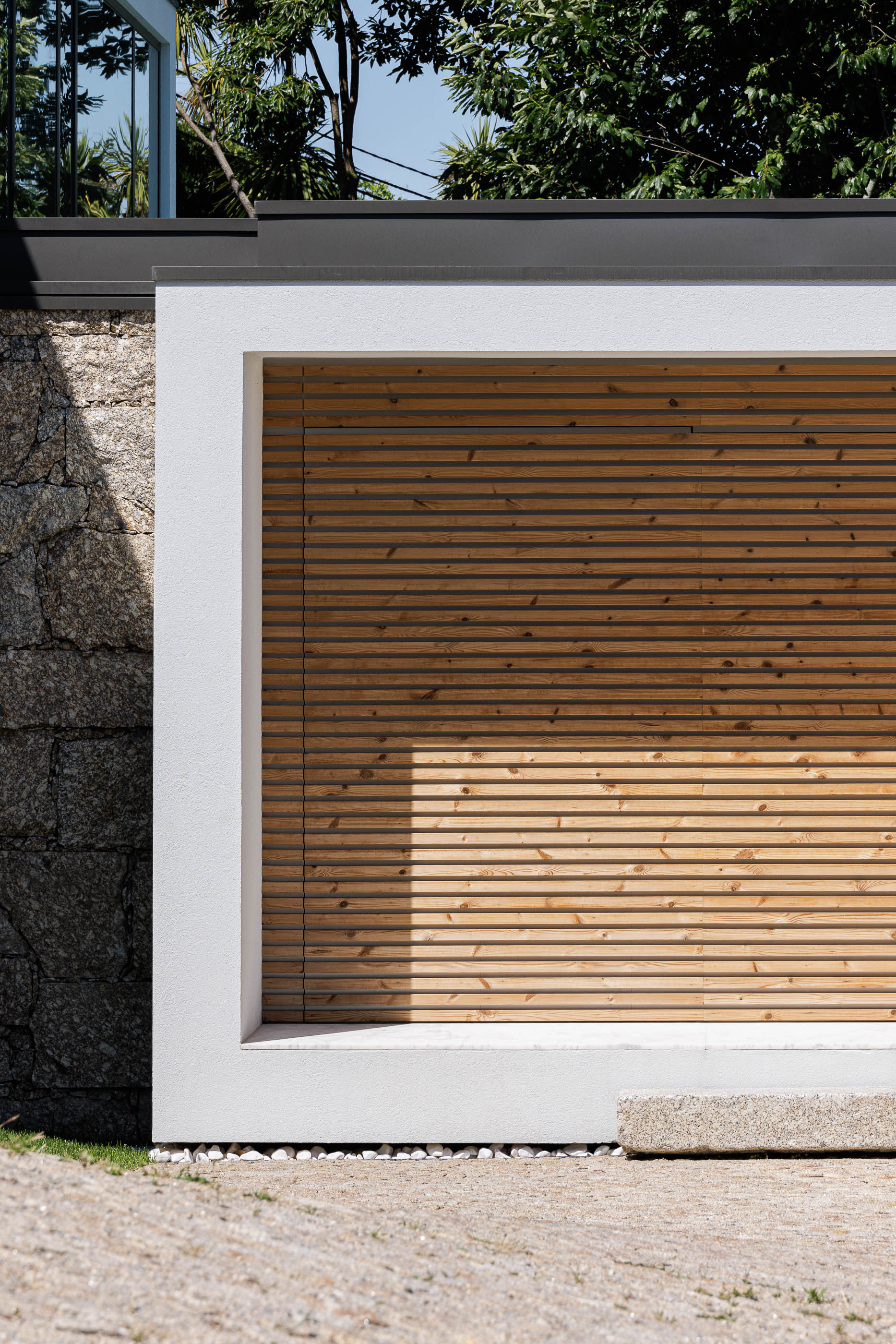 Exterior: Detalhe da fachada com revestimento em madeira horizontal e muro de pedra rústica. — CASA [EN]COSTA arquitetura Hous3 em Guimarães