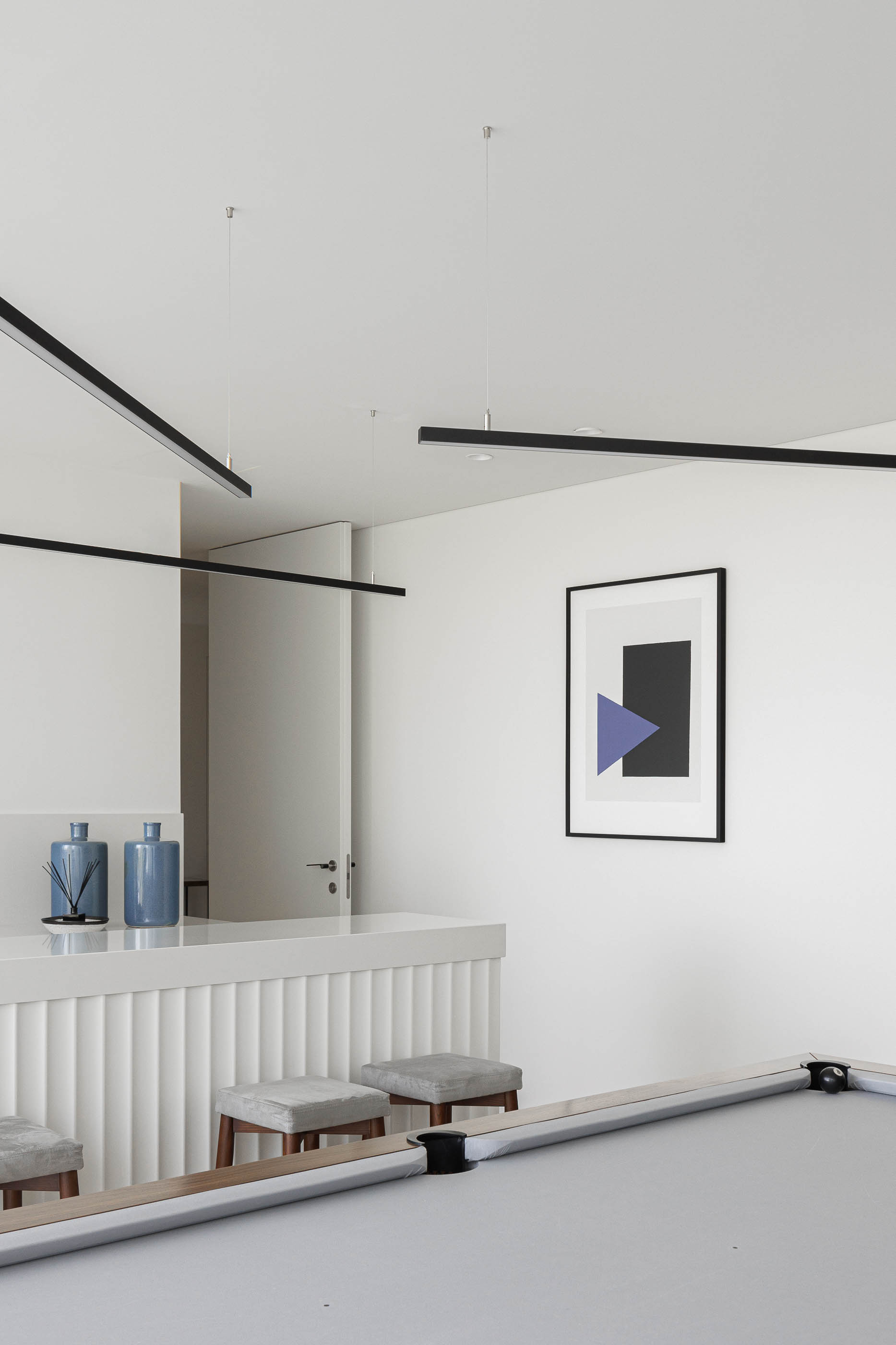 Sala de jogos: Mesa de bilhar, balcão branco com ripas verticais e candeeiros lineares suspensos. — CASA [EN]COSTA arquitetura Hous3 em Guimarães