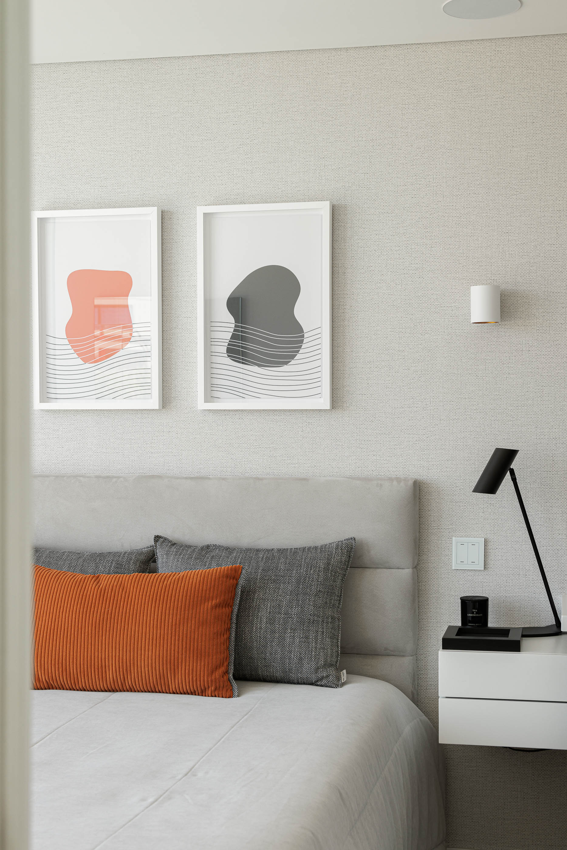 Quarto: Cama com cabeceira almofadada, mesa de cabeceira branca e candeeiro preto, quadros na parede. — CASA [EN]COSTA arquitetura Hous3 em Guimarães