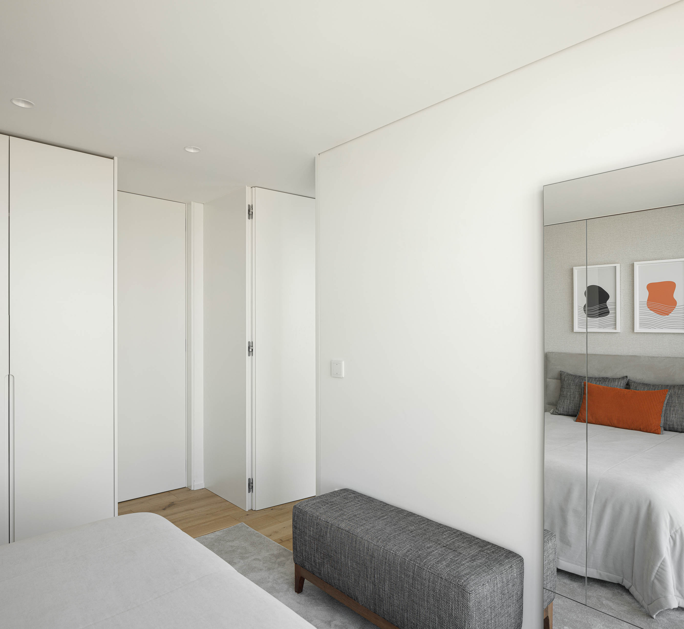 Quarto: Detalhe do quarto com roupeiro branco embutido, banco estofado e espelho amplo. — CASA [EN]COSTA arquitetura Hous3 em Guimarães