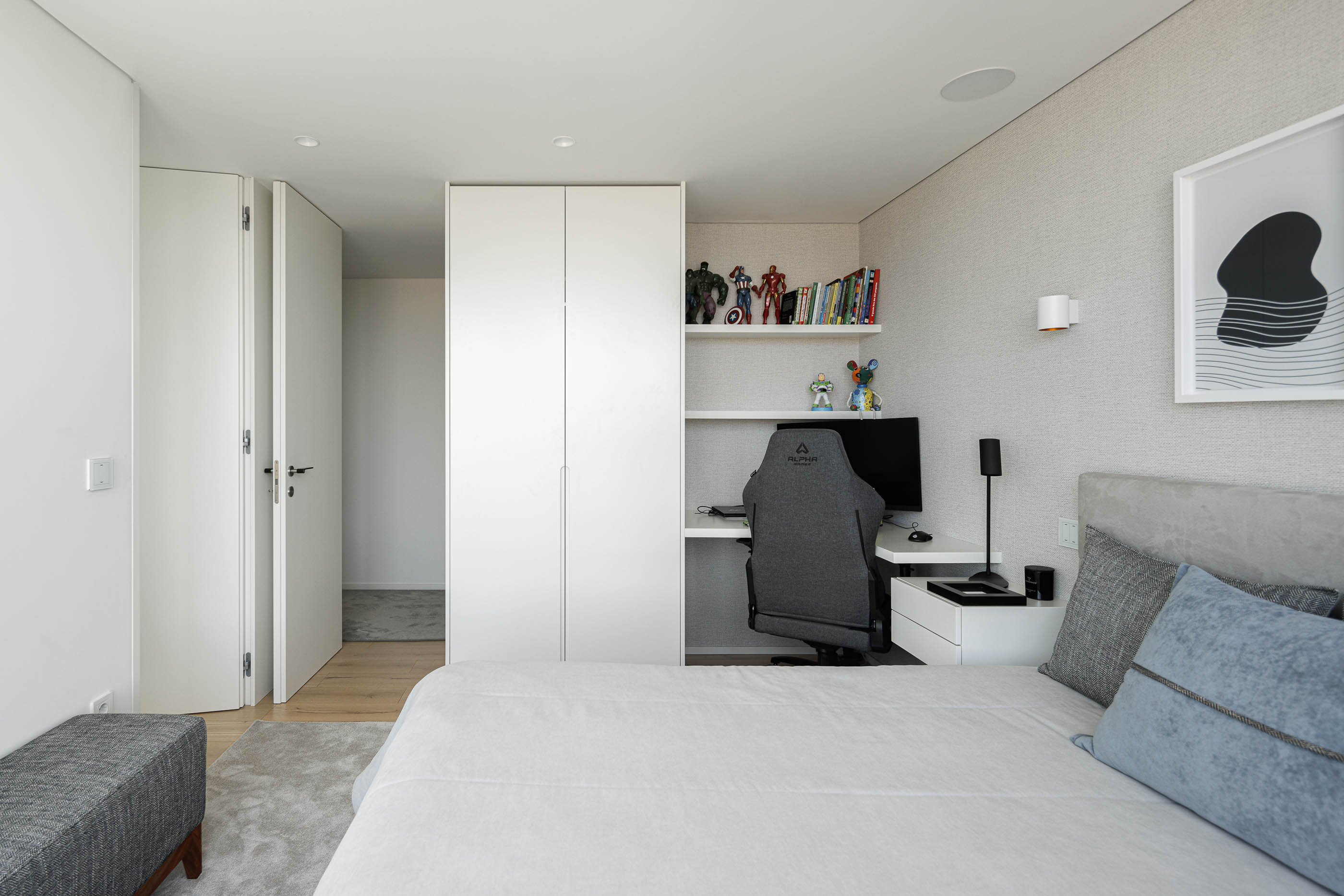 Quarto: Cama com roupa de cama clara, secretária com estantes e cadeira de gaming. — CASA [EN]COSTA arquitetura Hous3 em Guimarães