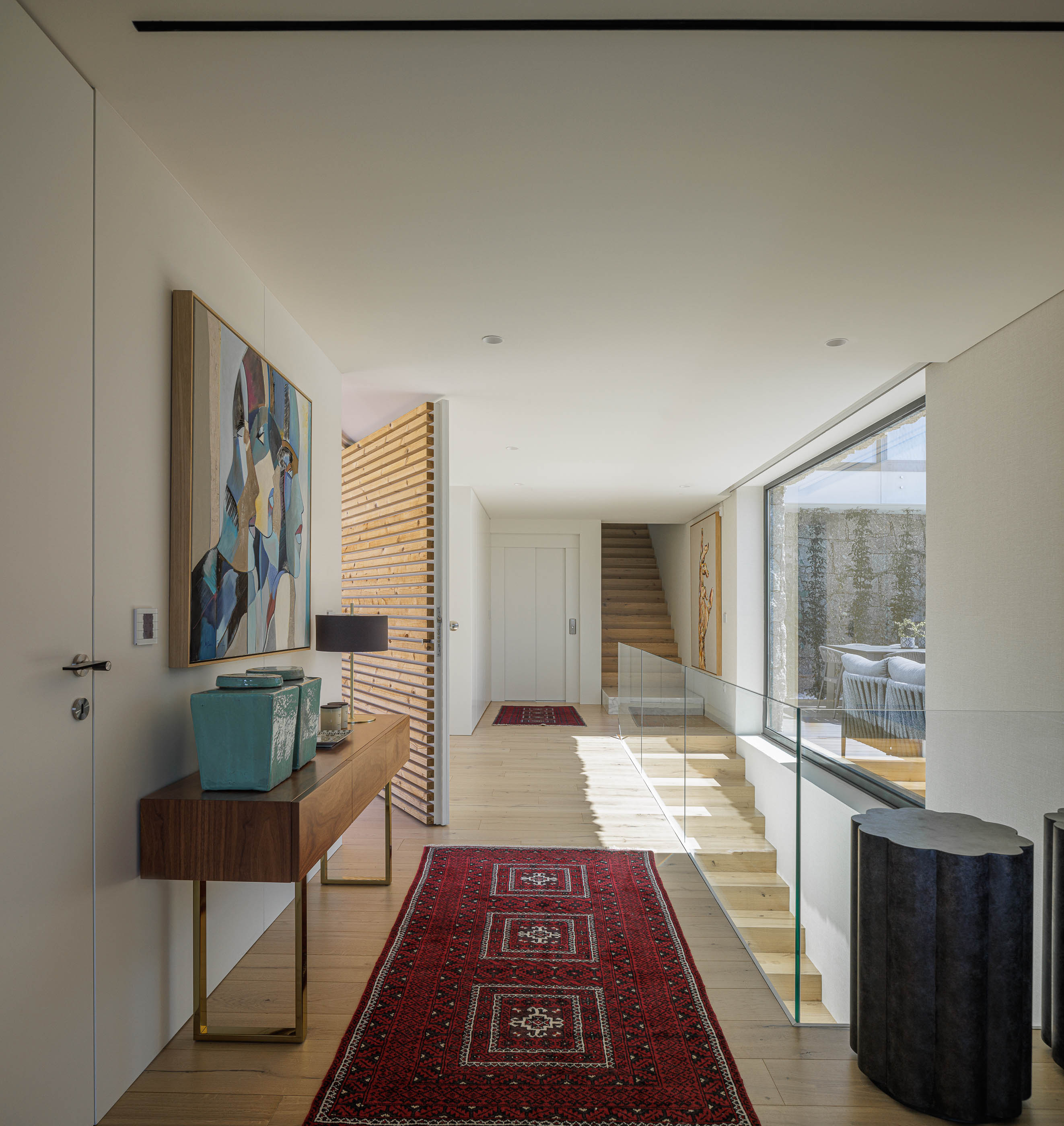 Corredor: Consola em madeira com candeeiro e objetos decorativos, alcatifa vermelha e escadas ao fundo. — CASA [EN]COSTA arquitetura Hous3 em Guimarães