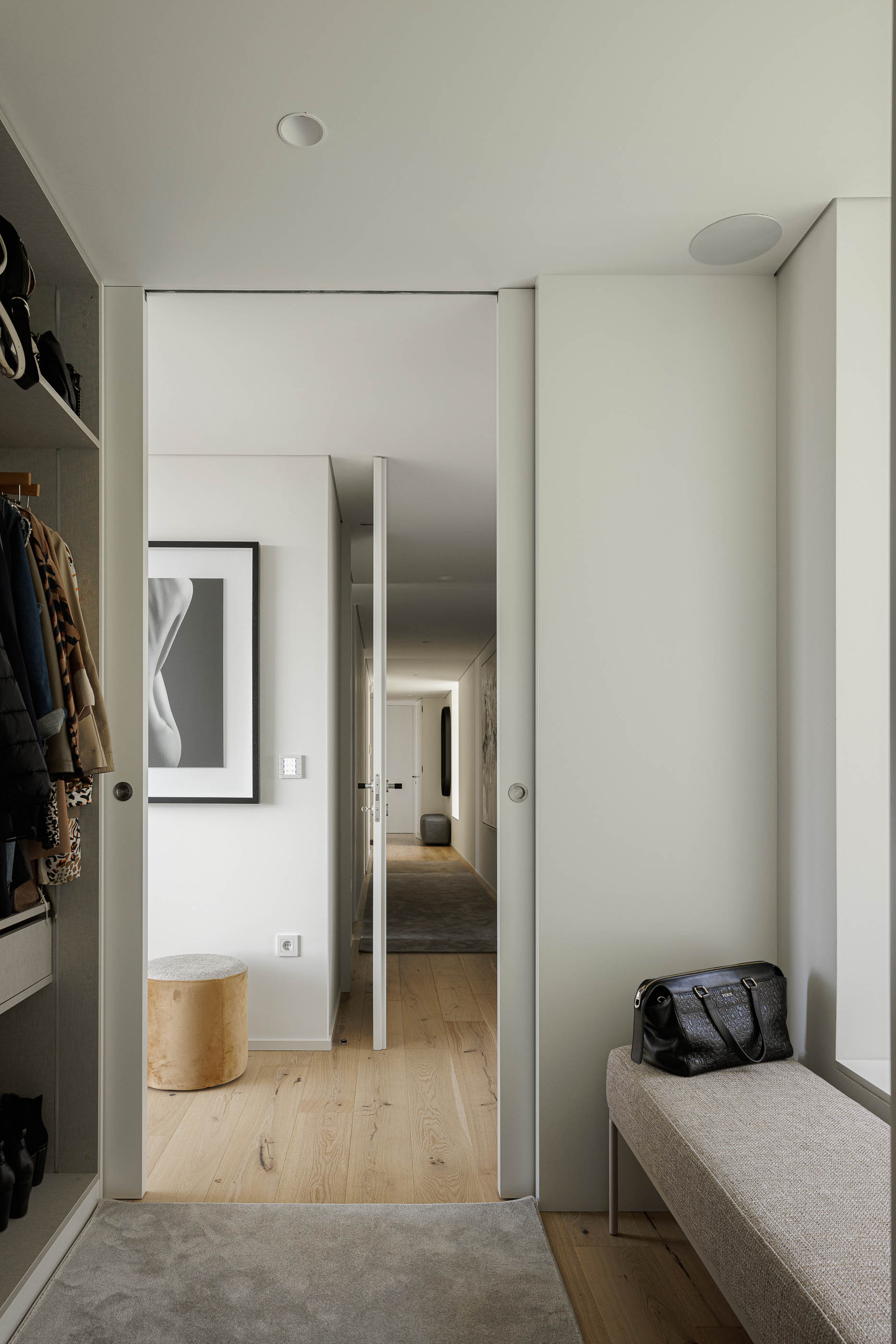 Closet: Roupeiro aberto com roupas penduradas, banco estofado e pavimento em madeira. — CASA [EN]COSTA arquitetura Hous3 em Guimarães