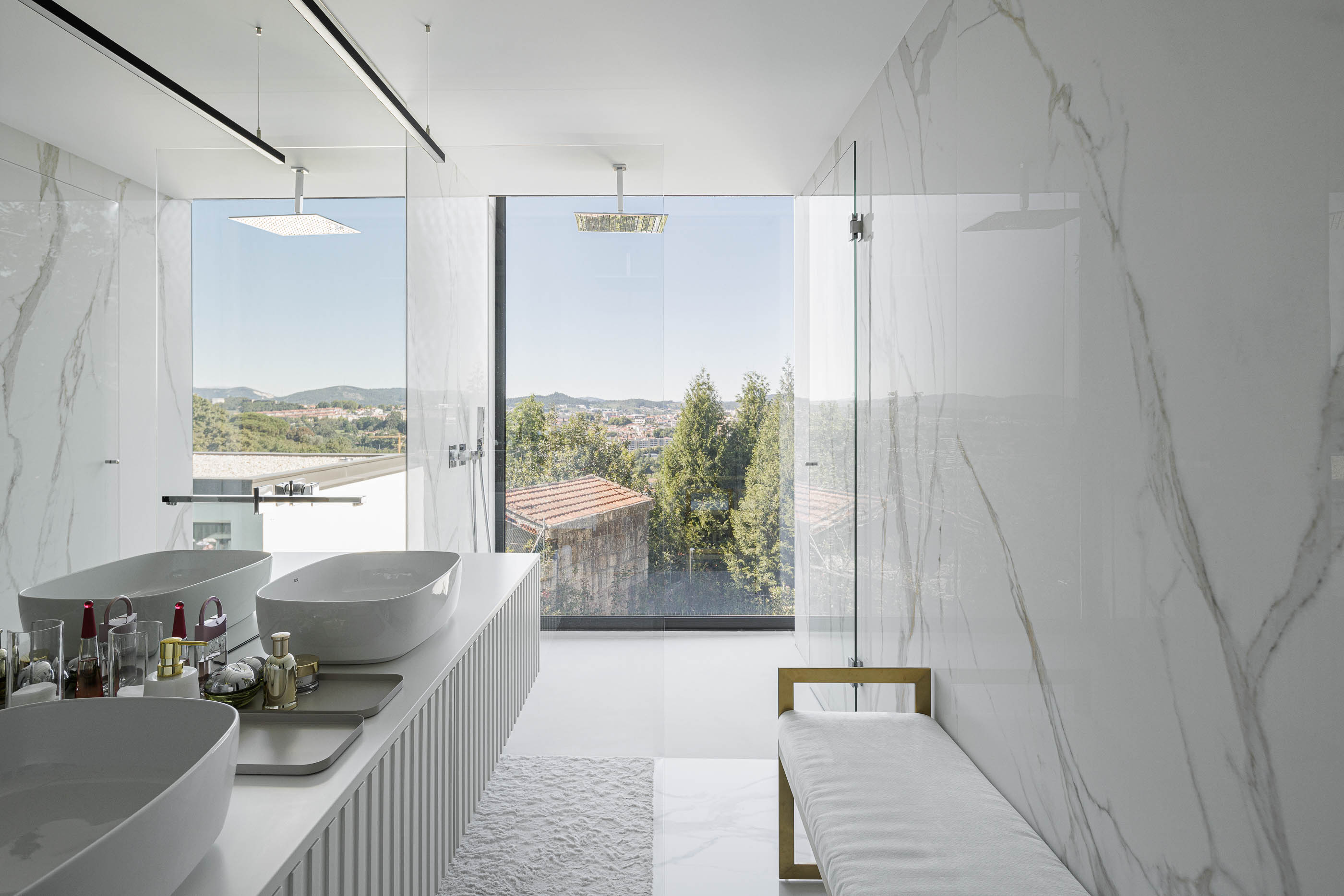 Casa de banho: Lavatórios duplos sobre móvel branco, espelhos amplos e duche com vista panorâmica. — CASA [EN]COSTA arquitetura Hous3 em Guimarães