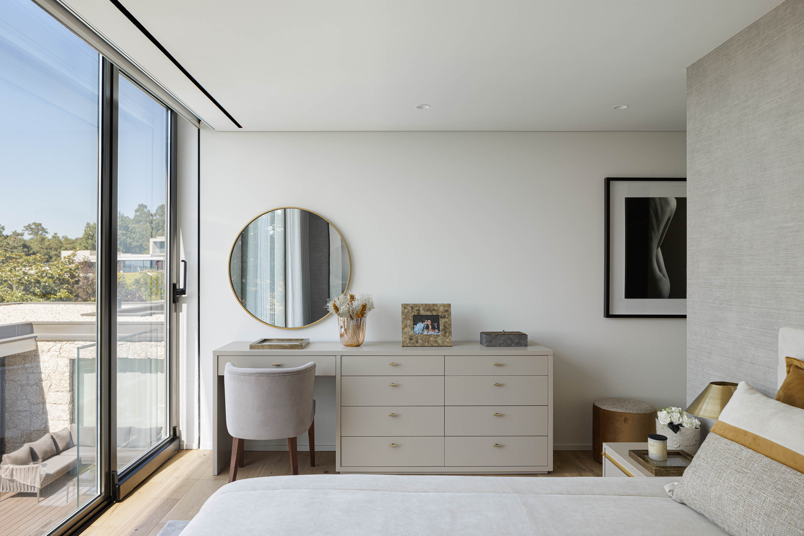 Quarto: Cama com vista para a varanda, toucador com espelho redondo e cadeira estofada. — CASA [EN]COSTA arquitetura Hous3 em Guimarães