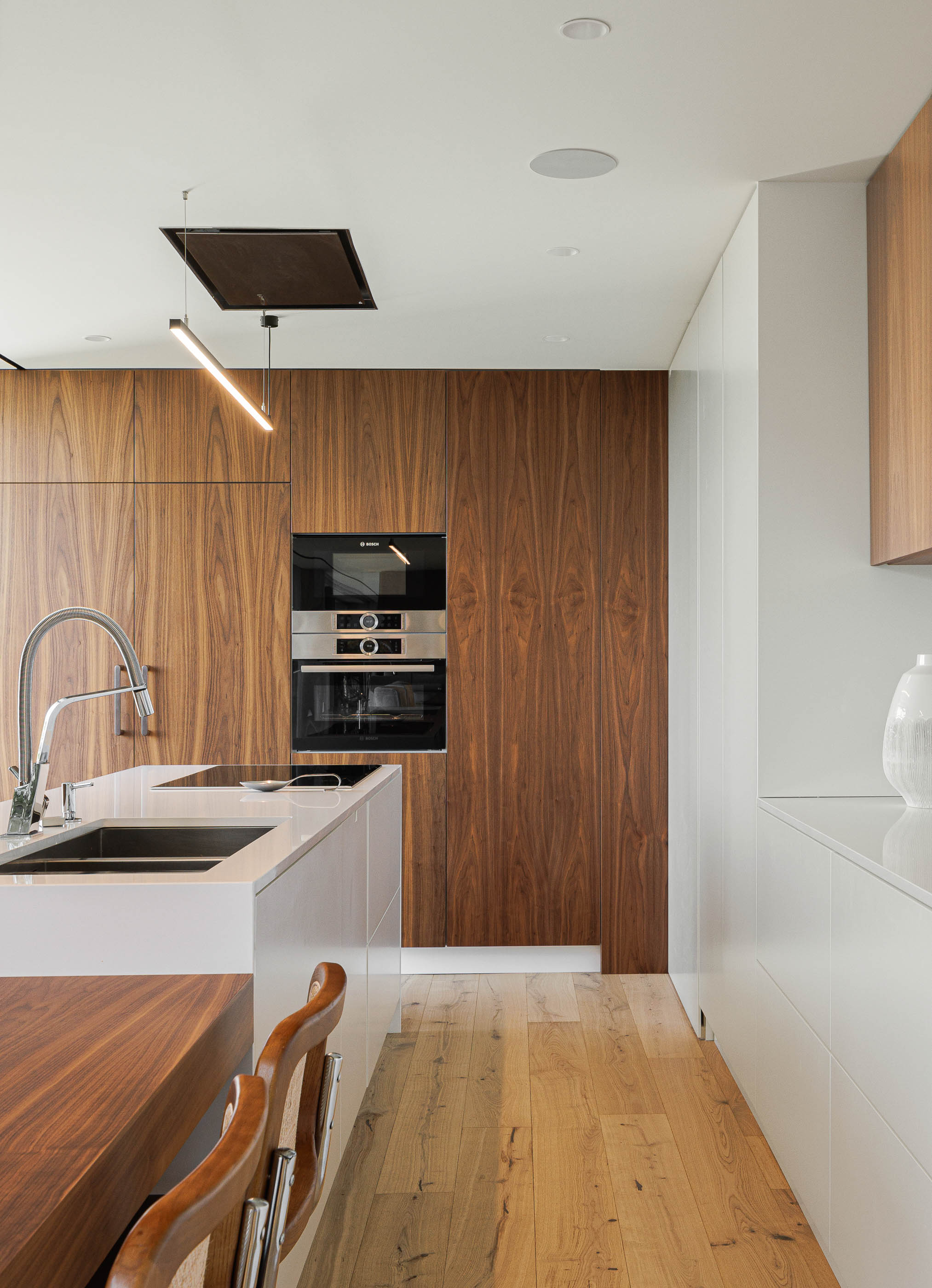 Cozinha: Armários em madeira escura e bancada branca com lava-loiça, pavimento em madeira clara. — CASA [EN]COSTA arquitetura Hous3 em Guimarães