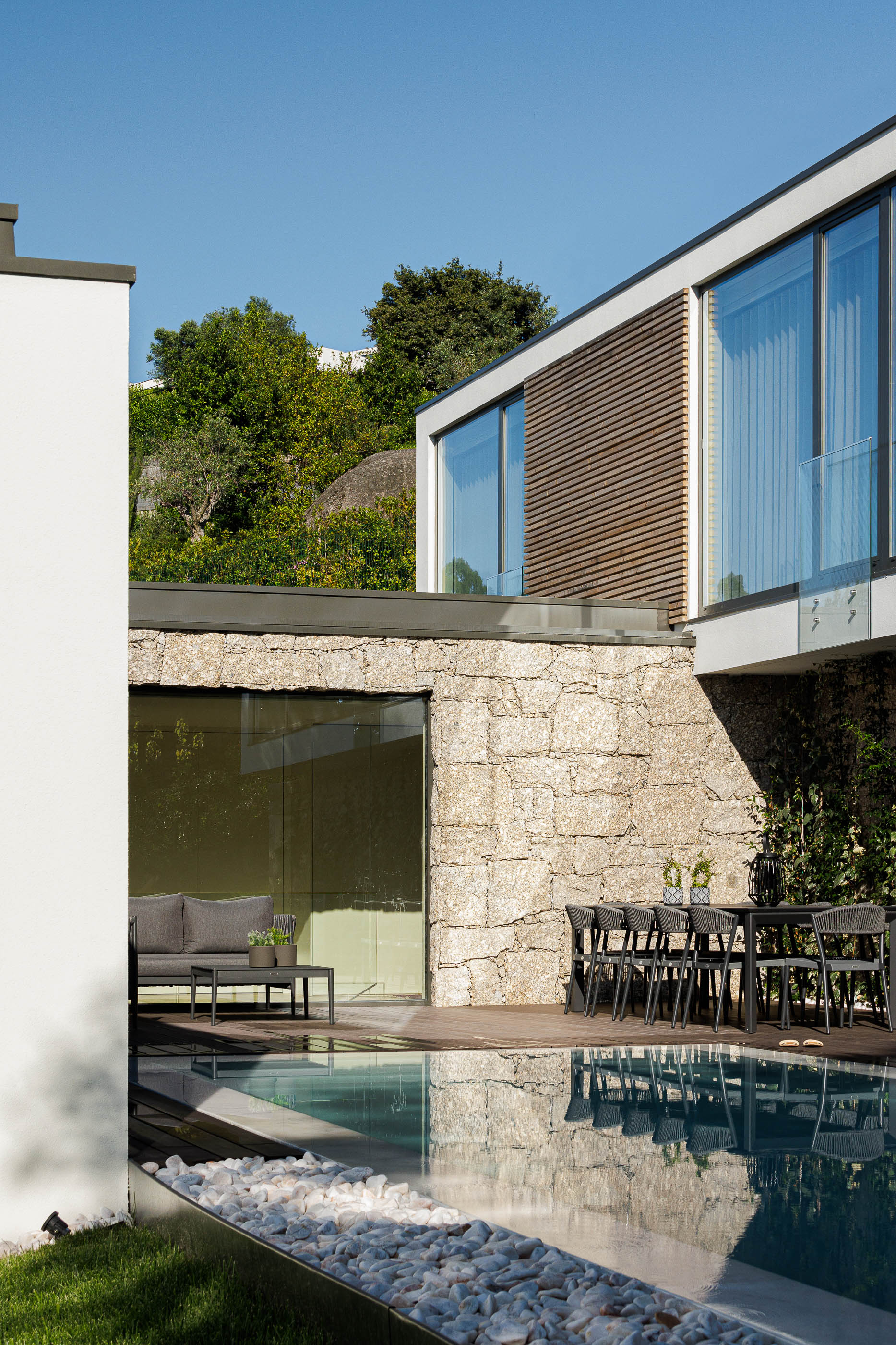 Exterior: Piscina com deck em madeira, zona de refeições e fachada em pedra. — CASA [EN]COSTA arquitetura Hous3 em Guimarães