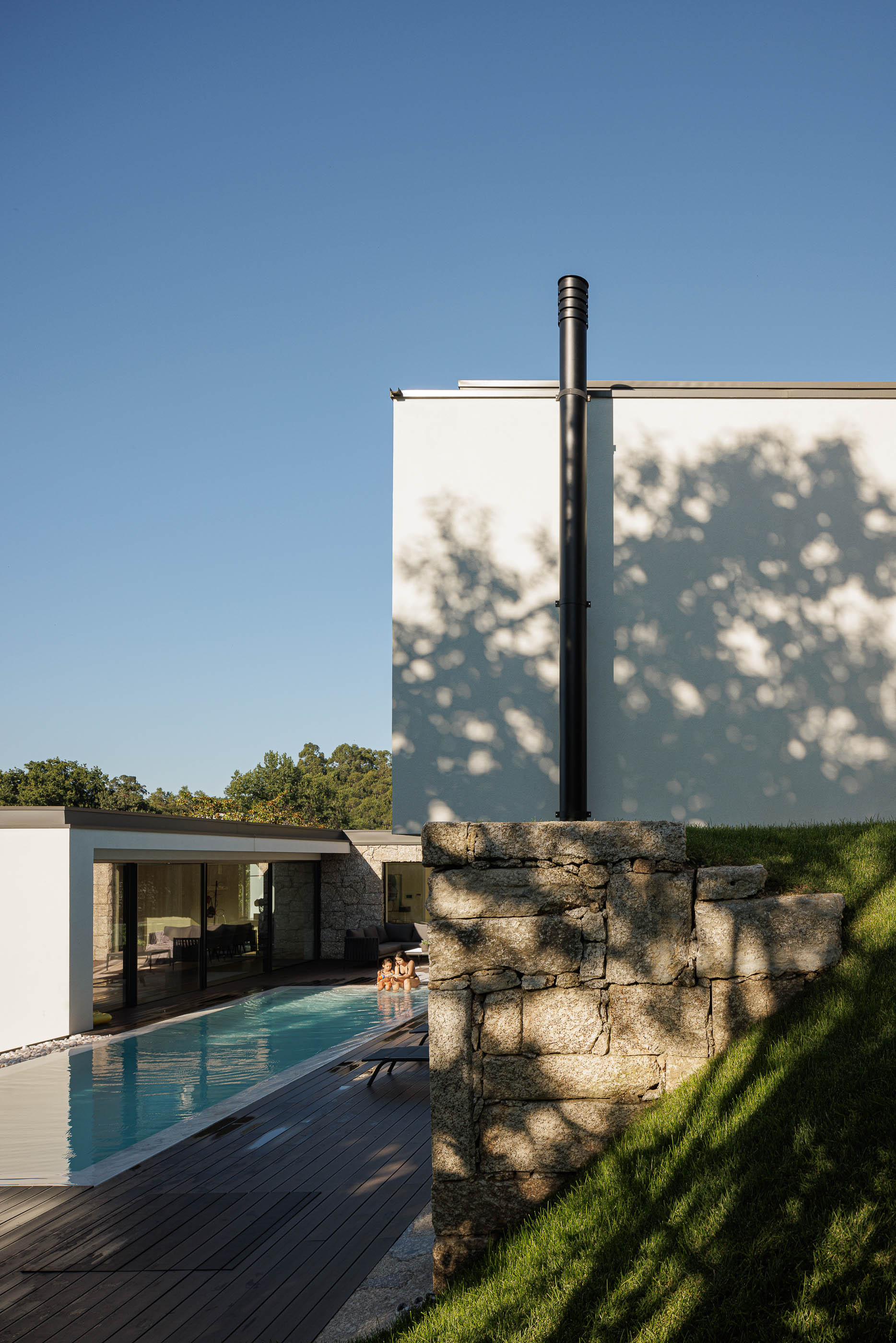 Exterior: Piscina com deck em madeira e fachada branca minimalista, com muros de pedra. — CASA [EN]COSTA arquitetura Hous3 em Guimarães