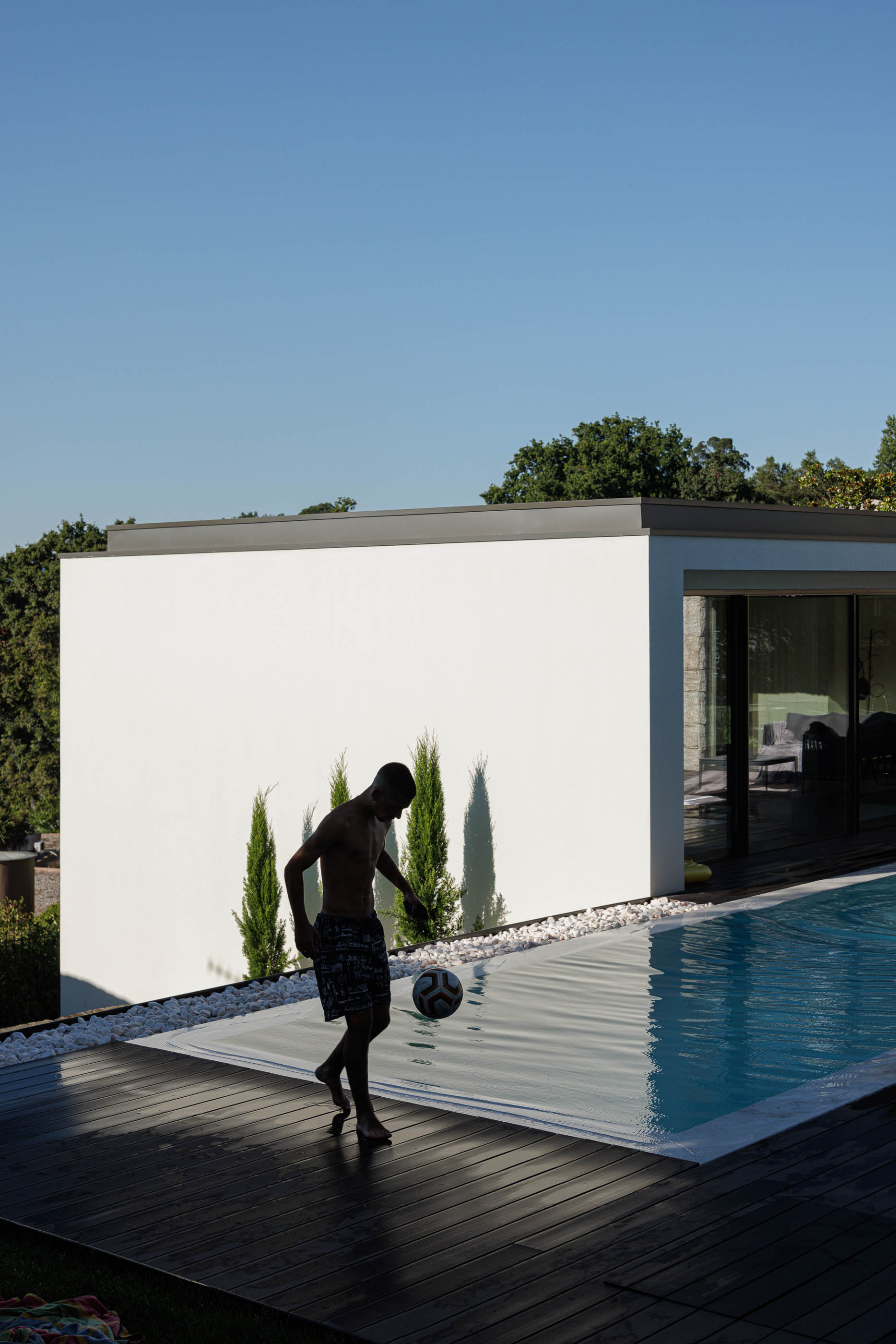 Exterior: Piscina com deck em madeira e fachada branca, com vegetação e árvores. — CASA [EN]COSTA arquitetura Hous3 em Guimarães