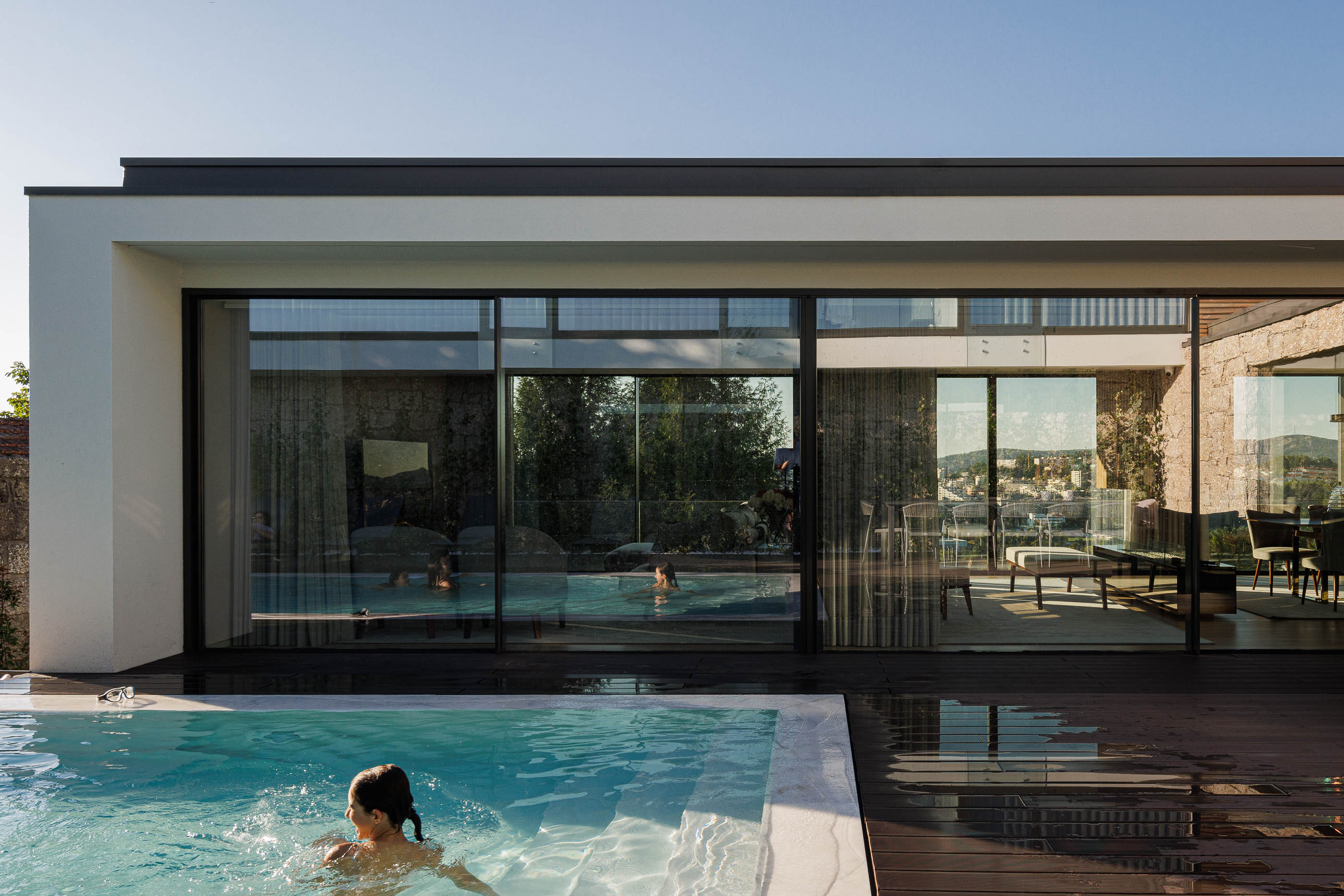 Exterior: Piscina com vista para a sala de jantar e estar, com deck em madeira. — CASA [EN]COSTA arquitetura Hous3 em Guimarães