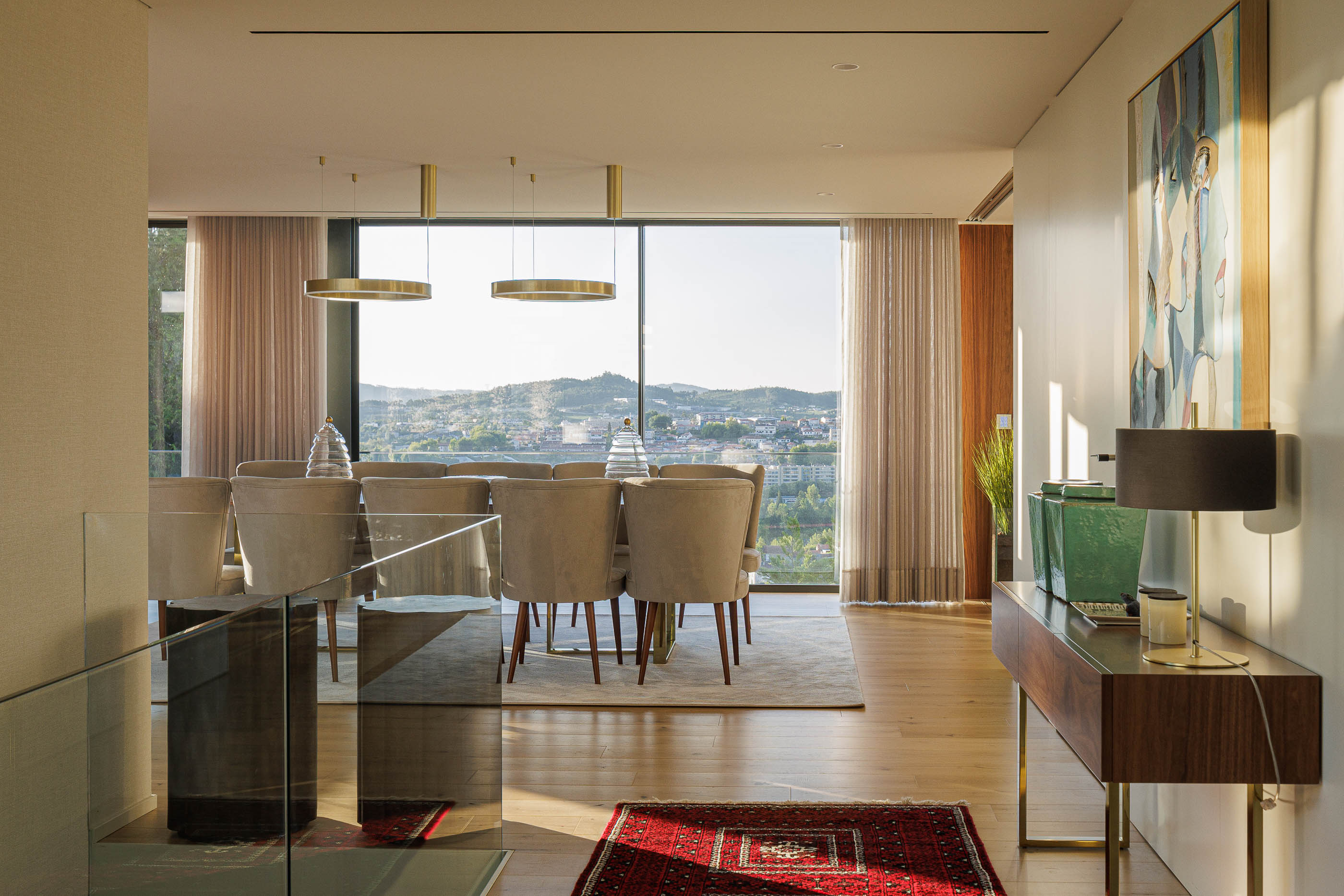 Sala de jantar: Mesa de jantar ampla com cadeiras estofadas, candeeiros suspensos e vista panorâmica. — CASA [EN]COSTA arquitetura Hous3 em Guimarães