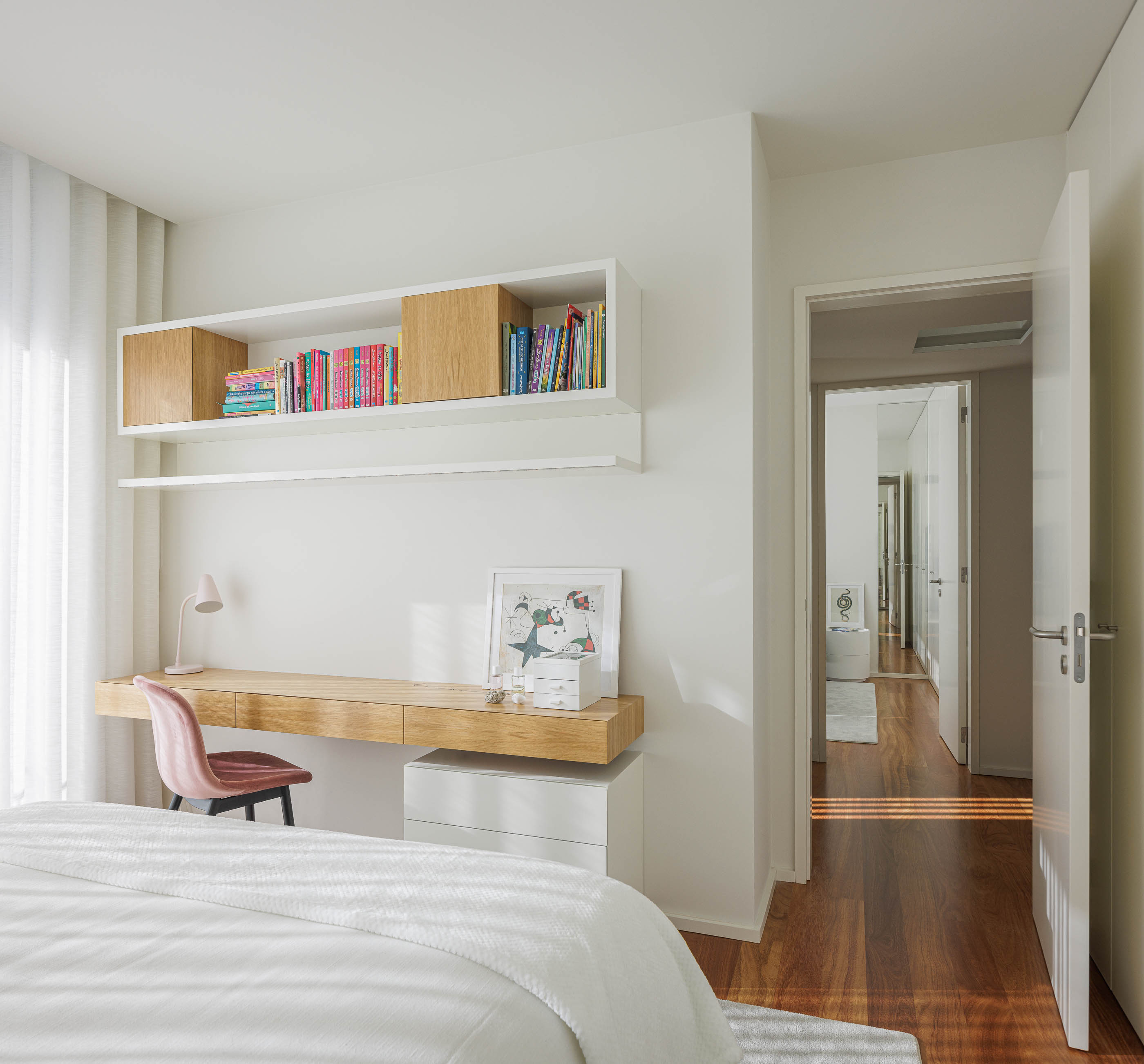 Quarto: Secretária suspensa com estantes, cadeira rosa e pavimento em madeira. — Casa R.P. arquitetura Atelier d´Arquitectura Lopes da Costa em Santa Maria da Feira