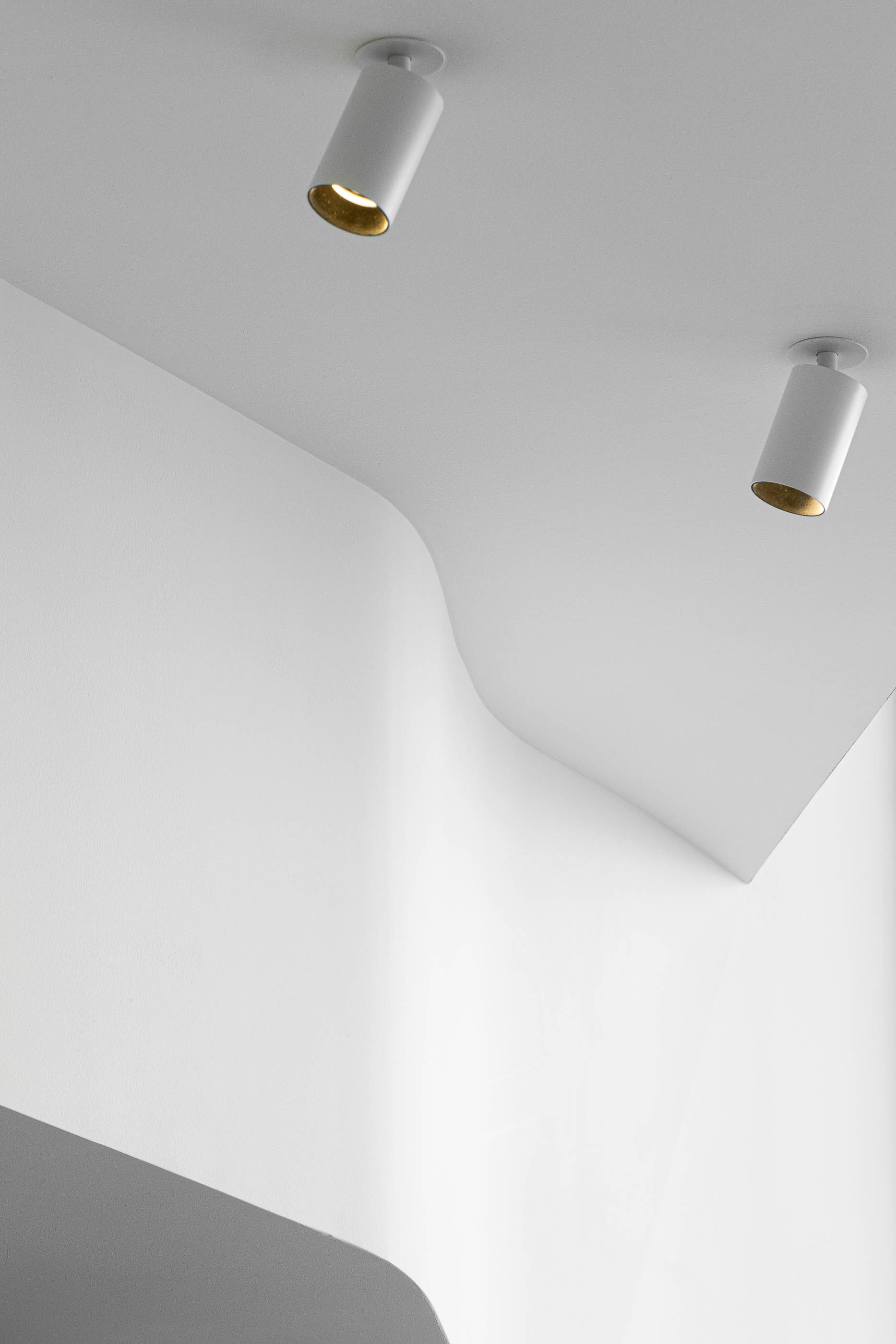 Teto: Detalhe do teto curvo branco com candeeiros cilíndricos. Design minimalista e iluminação focada. — Teresinha Carteiras Bolhão arquitetura Anarchlab Arquitectura em Porto