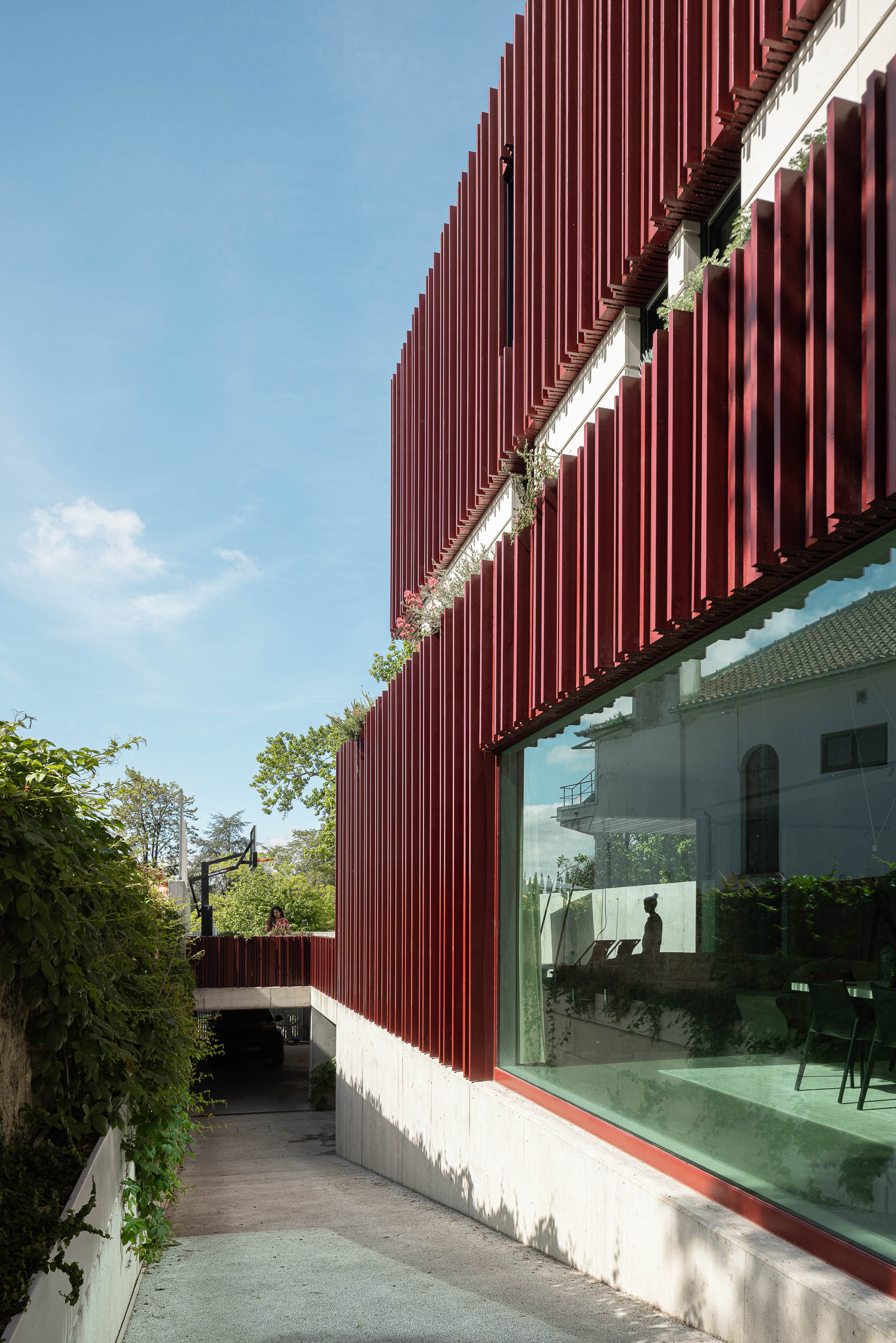 Exterior: Acesso à garagem subterrânea, fachada moderna com revestimento vermelho e grande janela. — Casa do Parque arquitetura Paulo Martins Arquitectura e Design em Aveiro