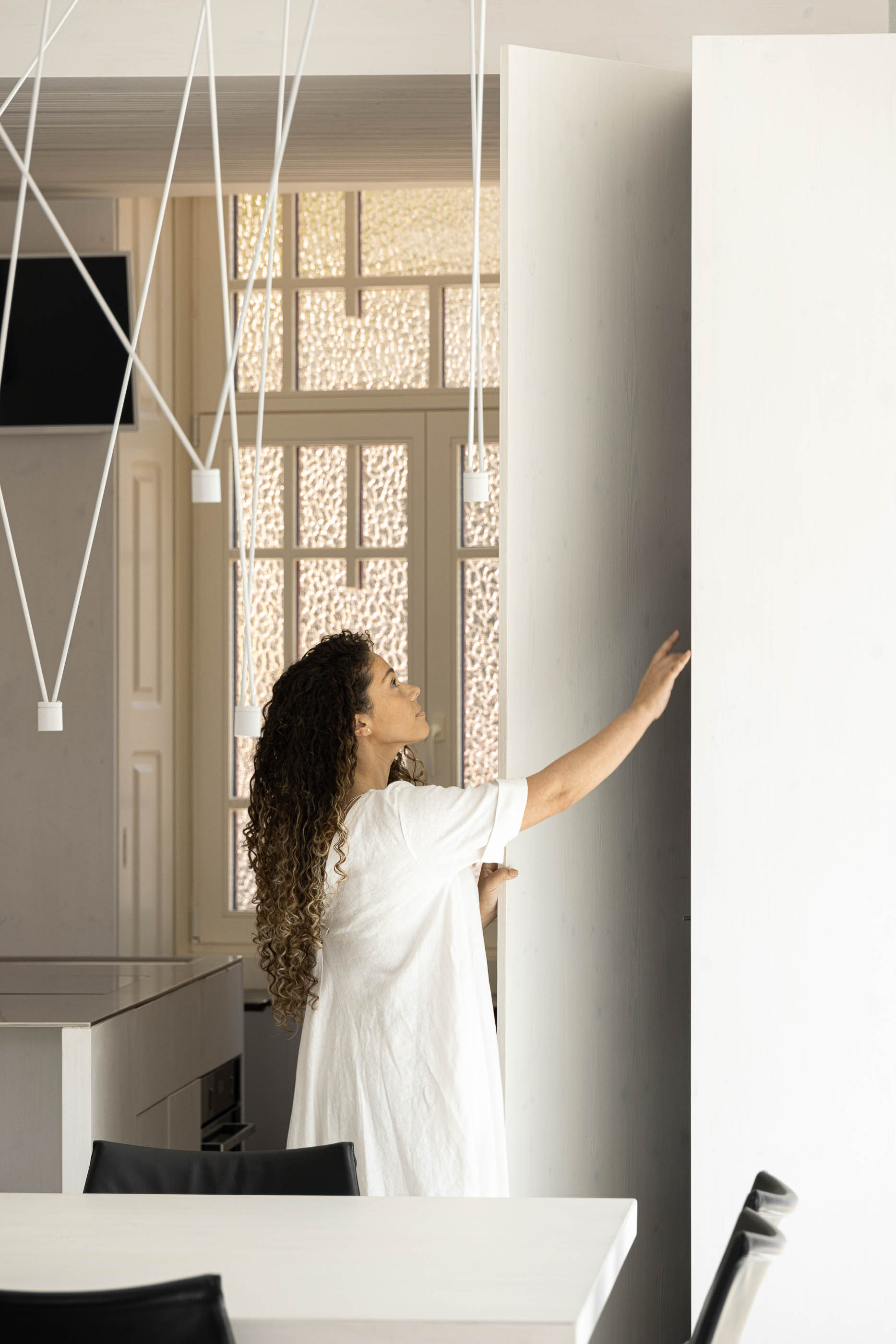 Cozinha: Detalhe da cozinha com candeeiros suspensos, armários brancos e porta antiga restaurada. — Casa do Parque arquitetura Paulo Martins Arquitectura e Design em Aveiro