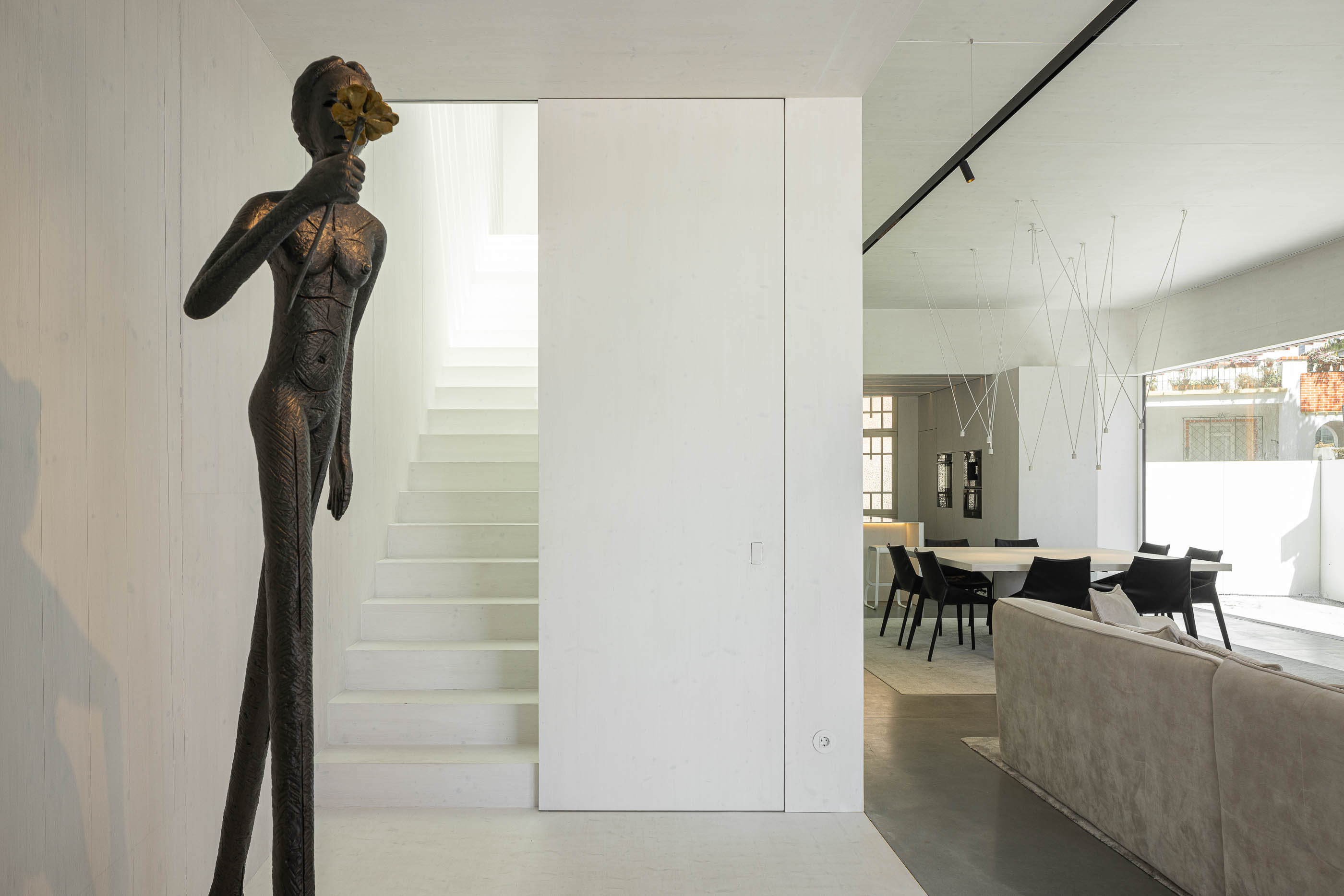 Hall de entrada: Escultura moderna, escadas brancas e vista para a sala de estar e jantar. — Casa do Parque arquitetura Paulo Martins Arquitectura e Design em Aveiro