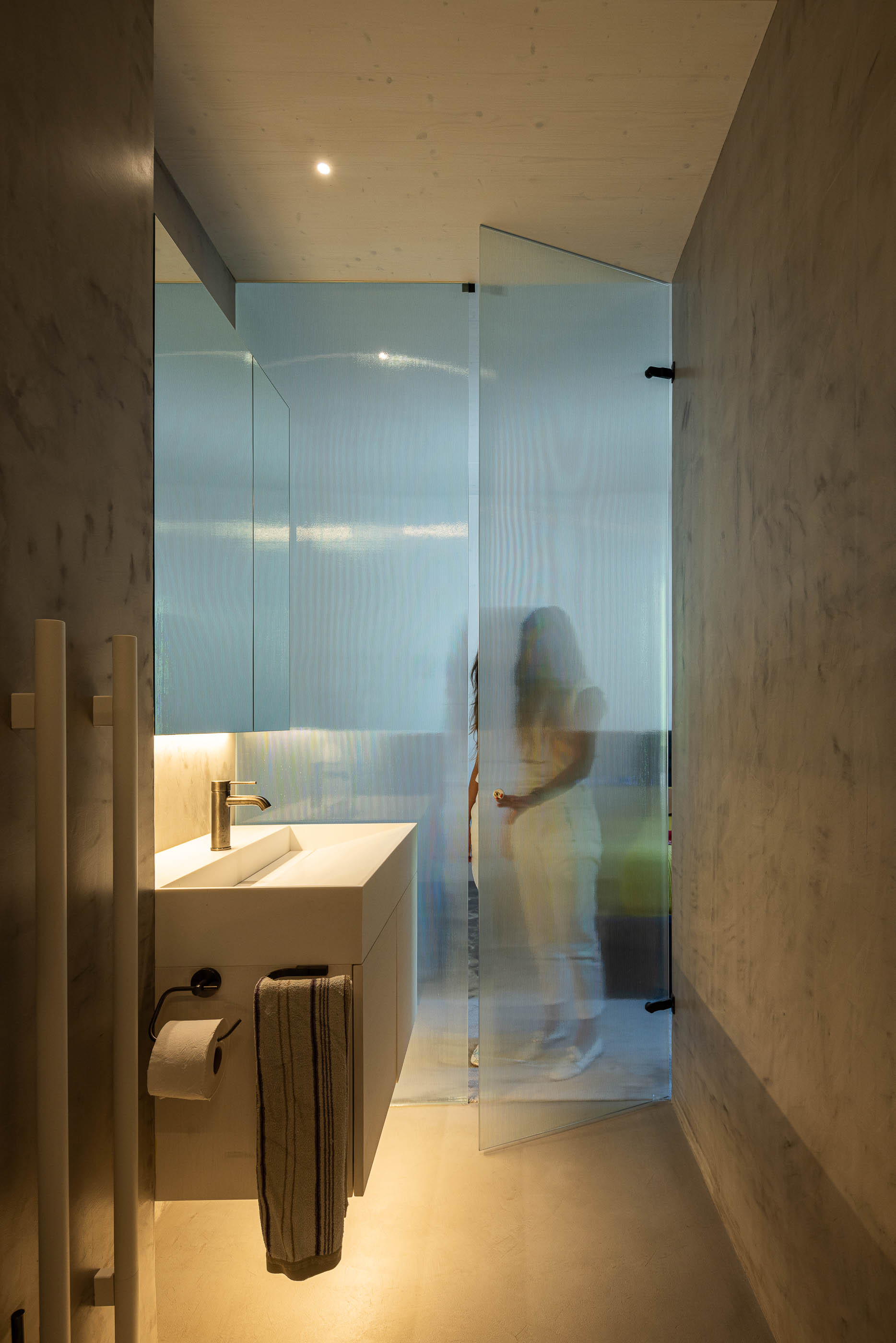 Casa de banho: Lavatório branco com torneira dourada, porta de vidro canelado e paredes cinzentas. — Casa do Parque arquitetura Paulo Martins Arquitectura e Design em Aveiro