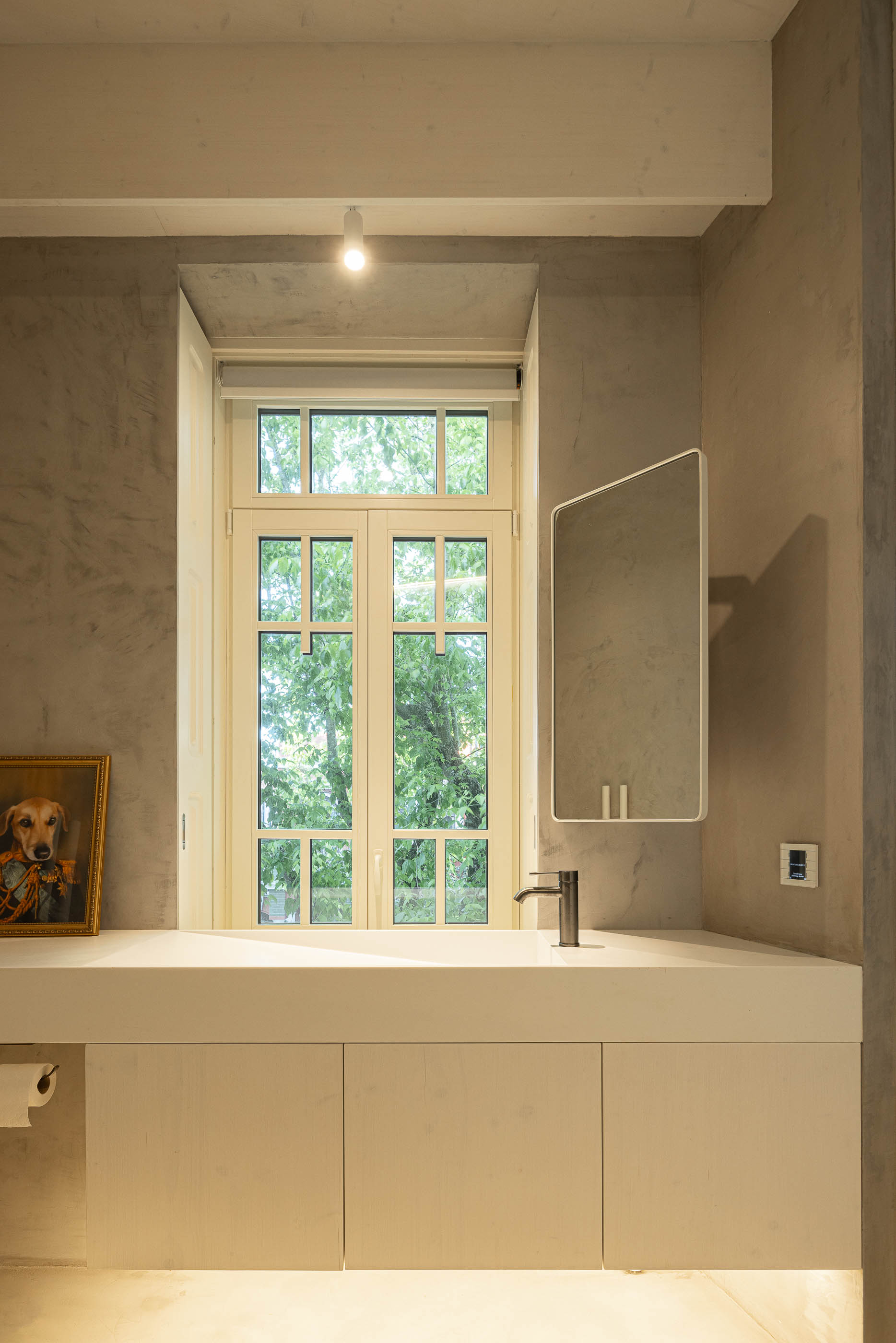 Casa de banho: Lavatório branco com espelho, janela antiga e paredes com acabamento em cimento. — Casa do Parque arquitetura Paulo Martins Arquitectura e Design em Aveiro