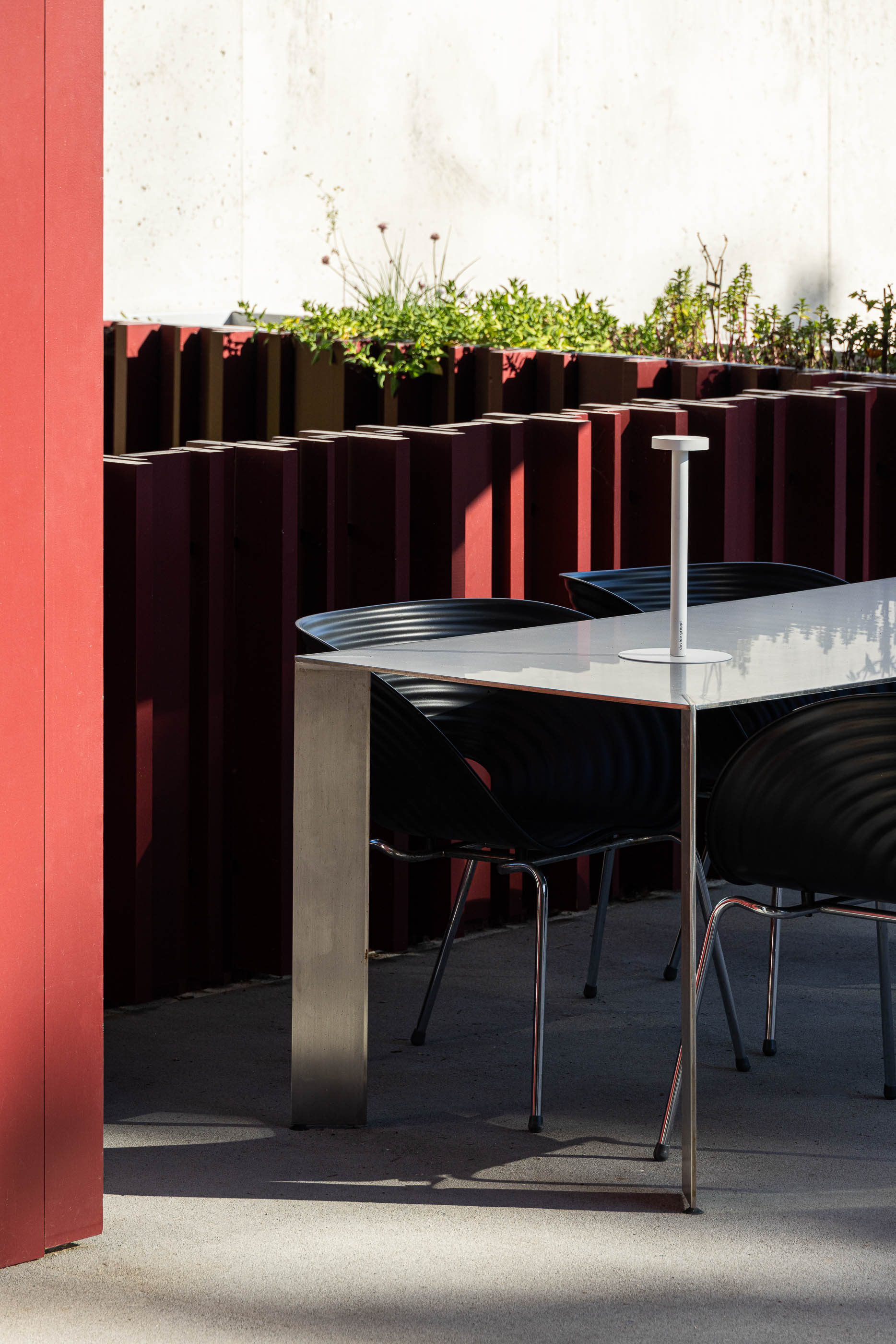 Exterior: Mesa de exterior com cadeiras pretas, revestimento vertical vermelho e vegetação. — Casa do Parque arquitetura Paulo Martins Arquitectura e Design em Aveiro