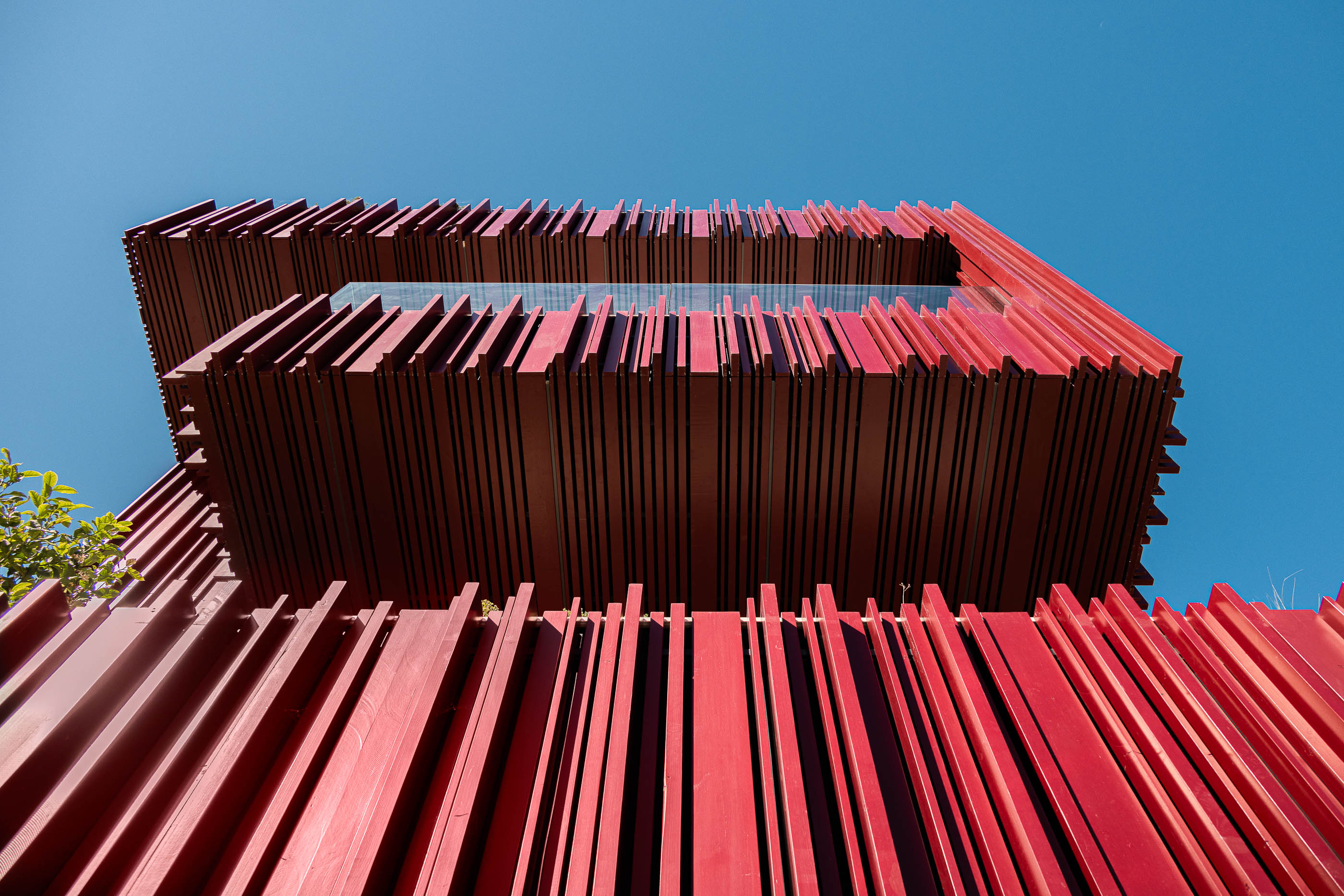 Exterior: Vista de baixo para cima da fachada com revestimento vertical vermelho e varandas. — Casa do Parque arquitetura Paulo Martins Arquitectura e Design em Aveiro