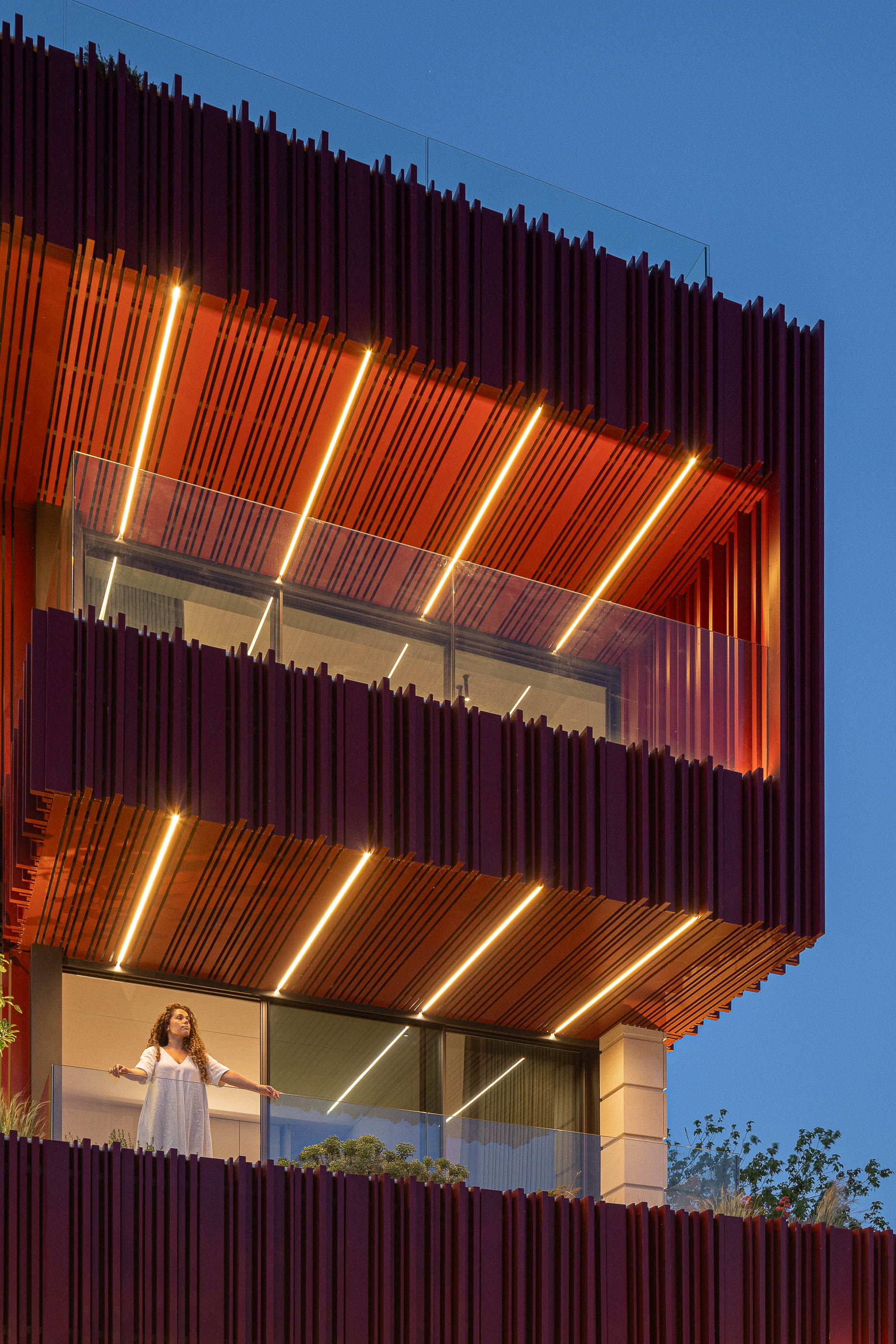 Fachada: Fachada com revestimento vertical vermelho iluminado, varandas com vegetação. — Casa do Parque arquitetura Paulo Martins Arquitectura e Design em Aveiro