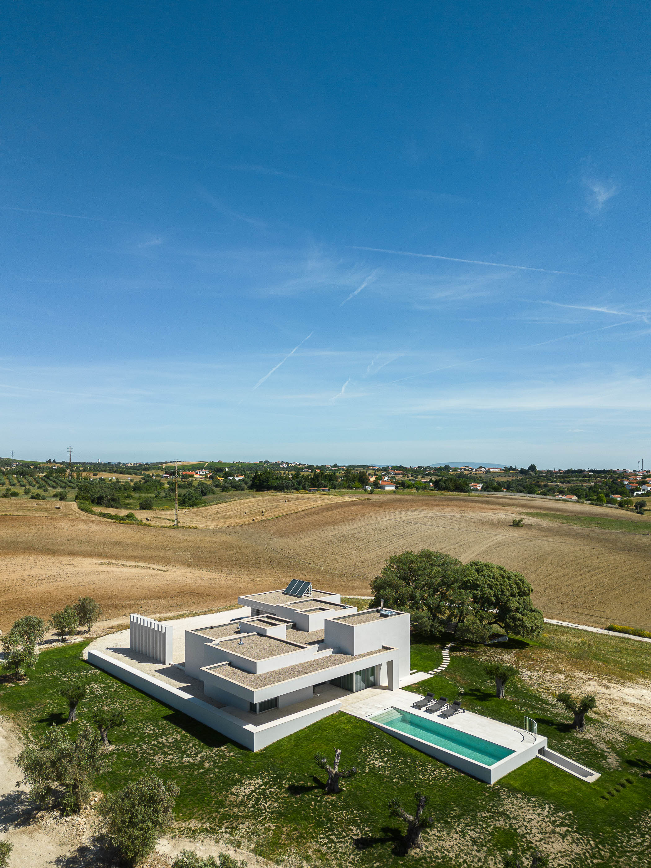 Exterior: Vista aérea da casa branca de arquitetura moderna, com piscina, inserida na paisagem rural de Santarém. — Casa na Romeira arquitetura dp arquitectos em Santarém