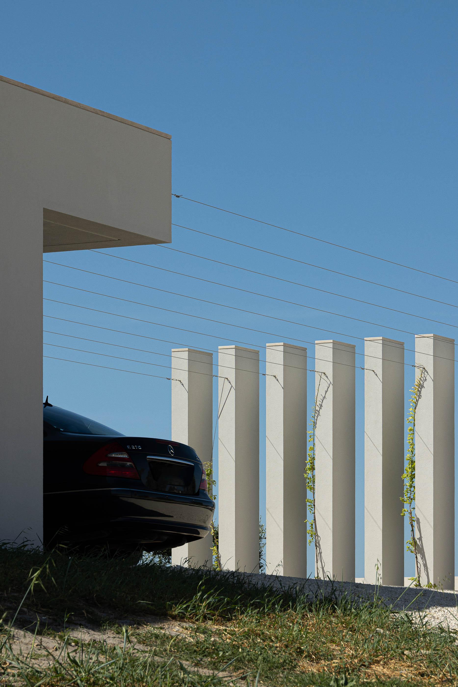 Garagem: Detalhe da garagem com portão cinzento, pilares verticais e um carro preto estacionado. — Casa na Romeira arquitetura dp arquitectos em Santarém
