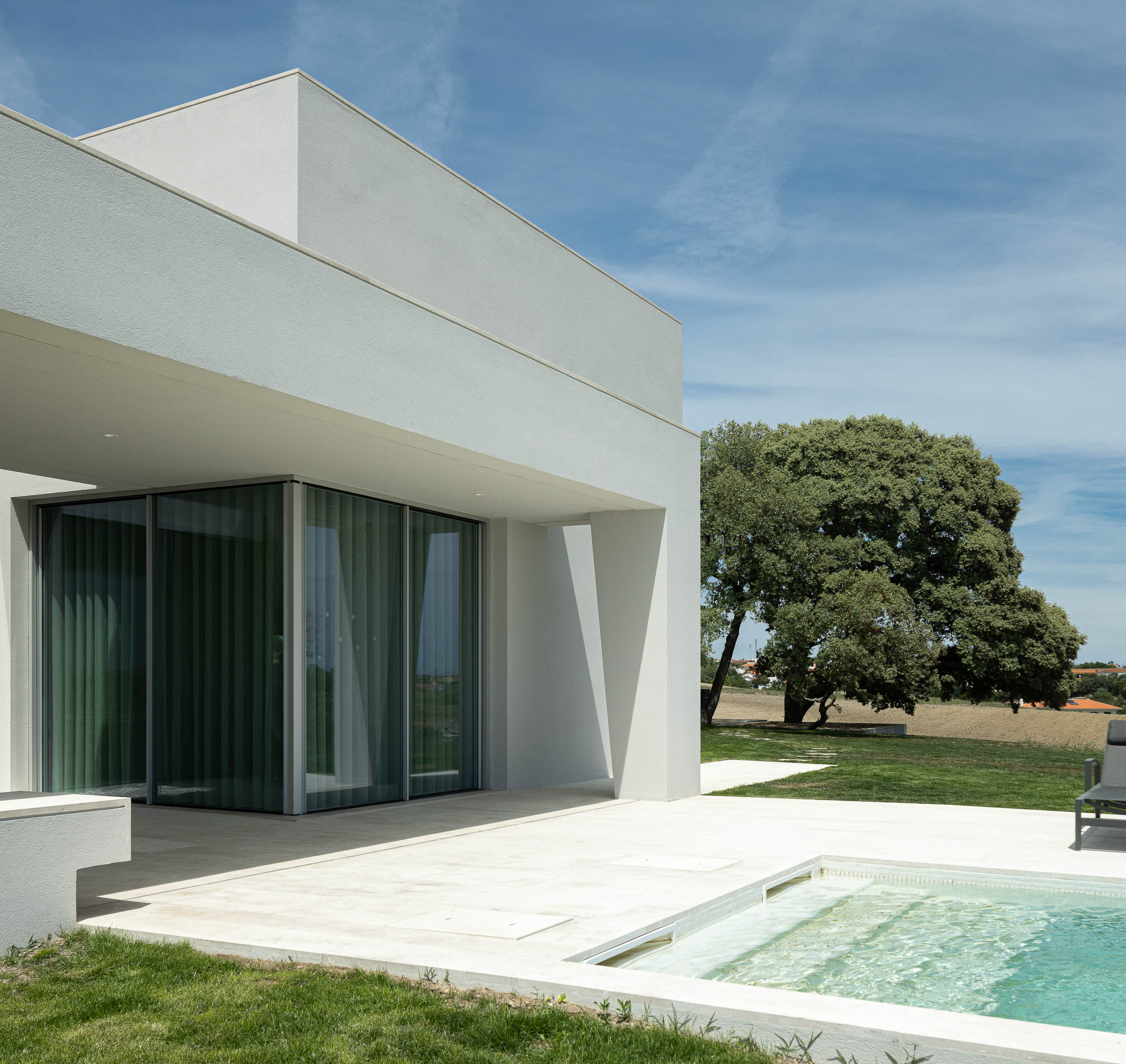 Piscina: Alpendre com grandes janelas de vidro, piscina com zona de baixa profundidade e relvado. — Casa na Romeira arquitetura dp arquitectos em Santarém