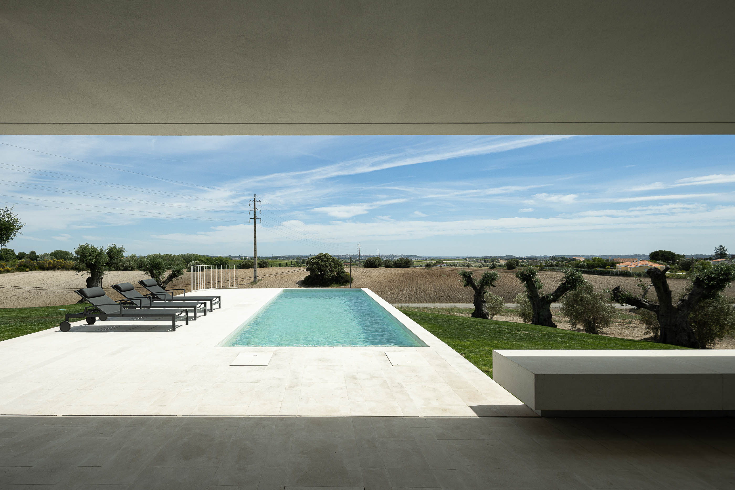 Cozinha: Cozinha moderna com armários brancos, bancada em pedra cinzenta e pavimento cerâmico. — Casa na Romeira arquitetura dp arquitectos em Santarém