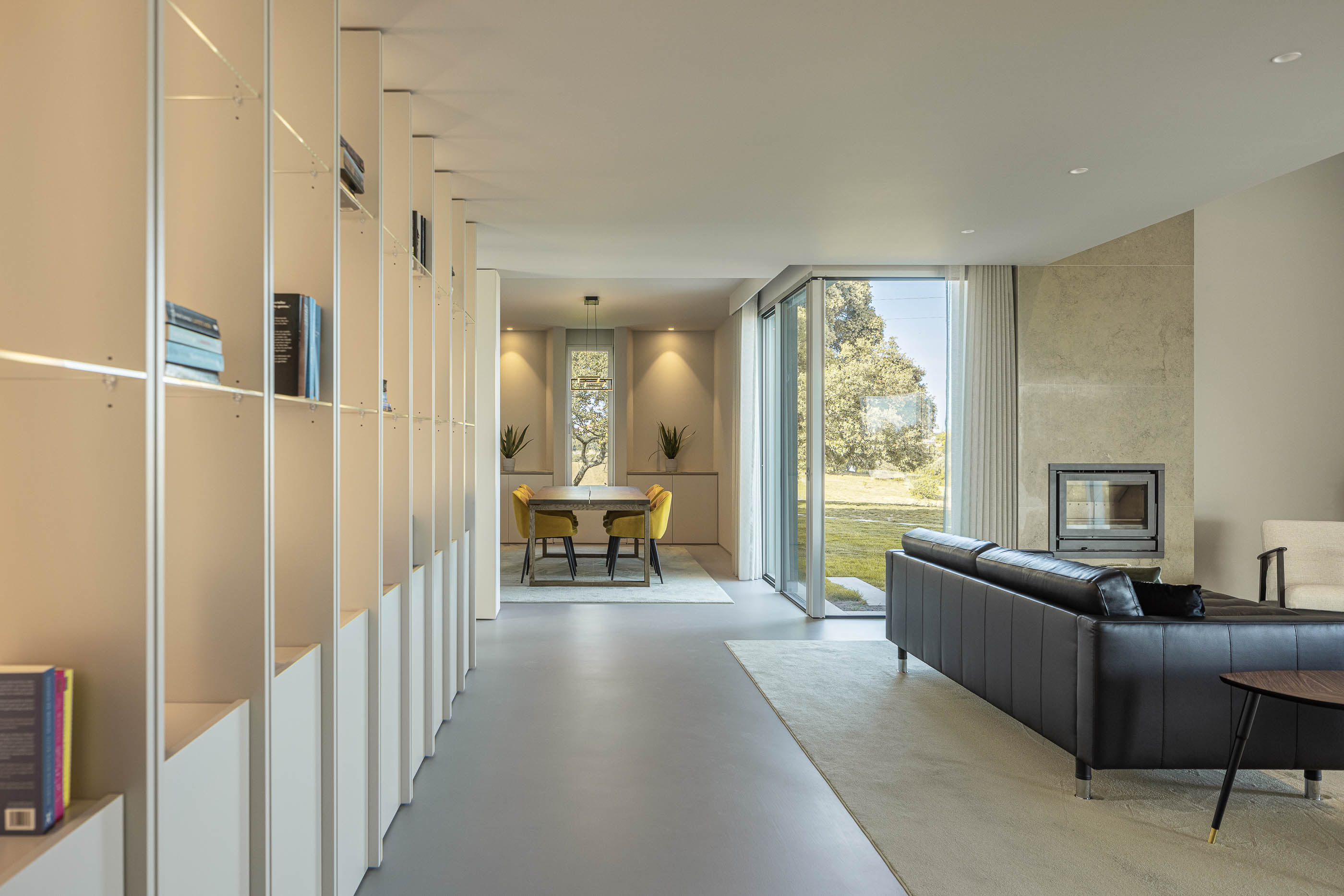 Sala de estar: Vista da sala de estar para a zona de refeições e piscina, com estantes brancas iluminadas. — Casa na Romeira arquitetura dp arquitectos em Santarém