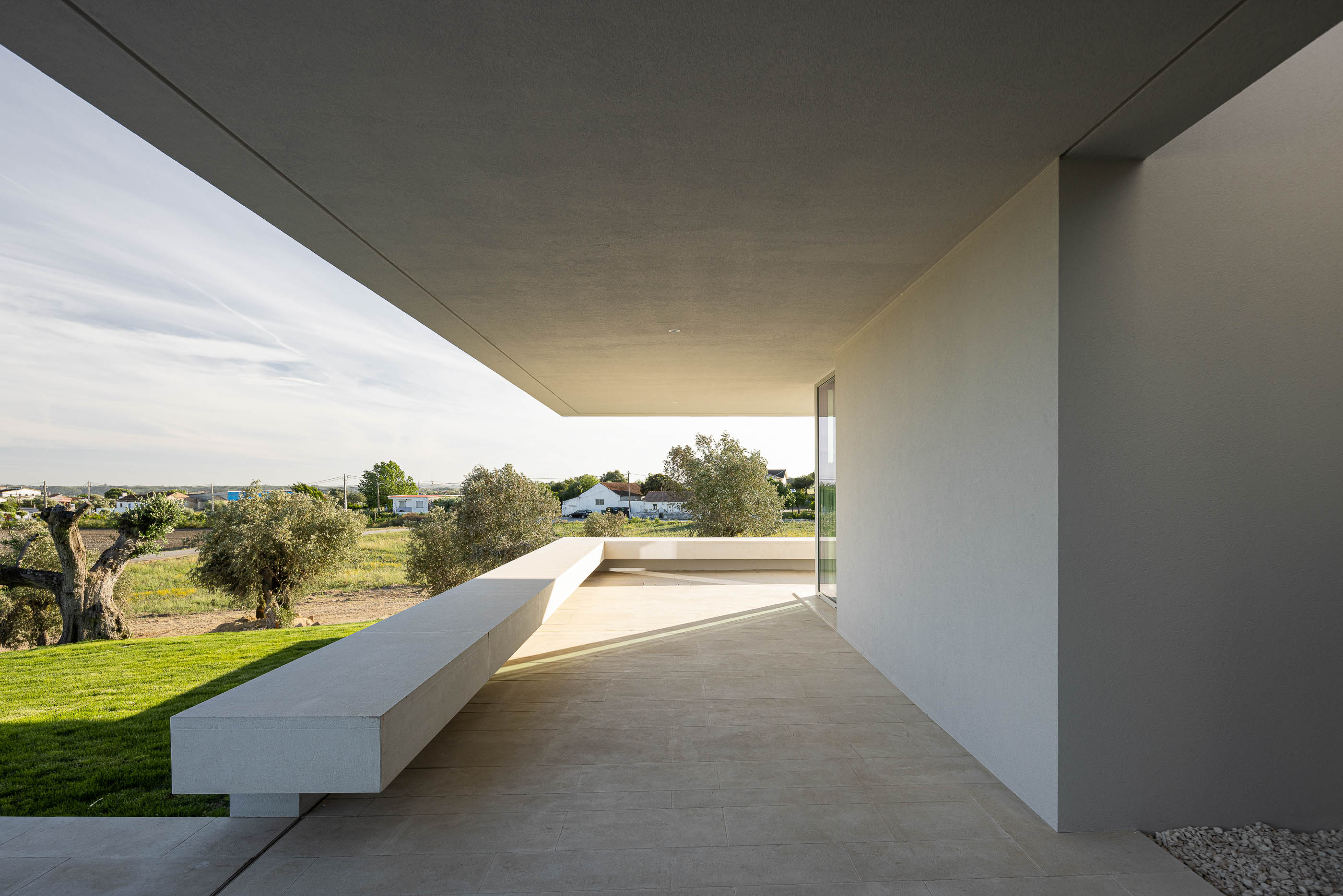 Exterior: Detalhe da fachada branca da casa com janelas de vidro e pilares verticais. — Casa na Romeira arquitetura dp arquitectos em Santarém