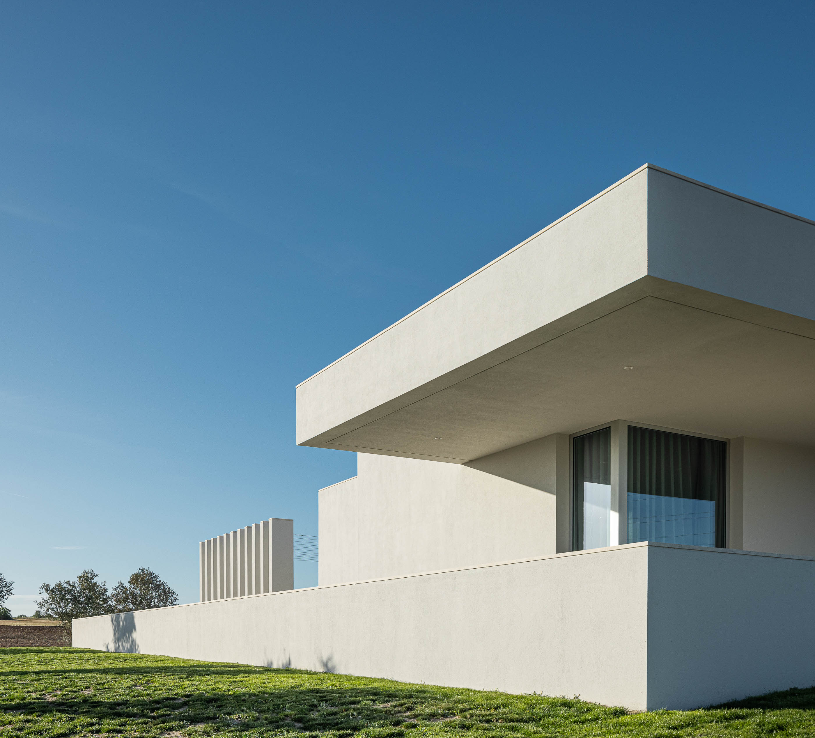 Exterior: Vista frontal da casa branca com garagem, entrada principal e jardim de seixo branco. — Casa na Romeira arquitetura dp arquitectos em Santarém