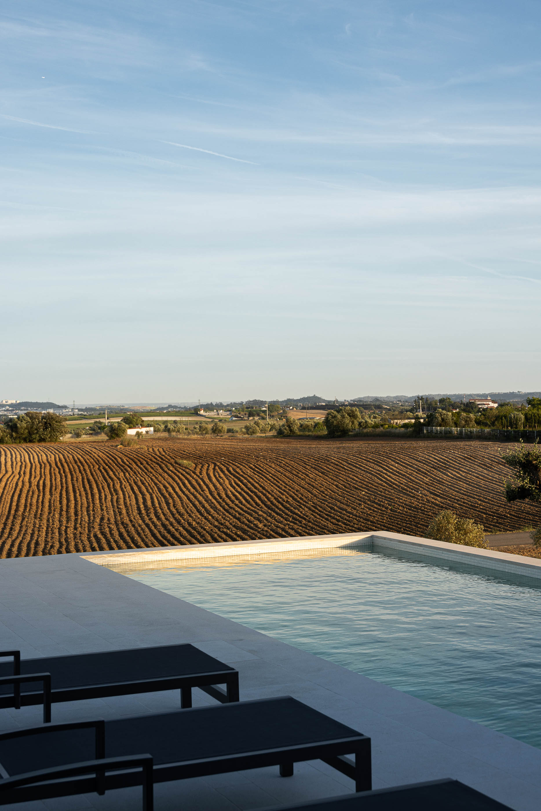 Piscina: Detalhe da piscina com escadas de acesso e vista para a paisagem rural. — Casa na Romeira arquitetura dp arquitectos em Santarém