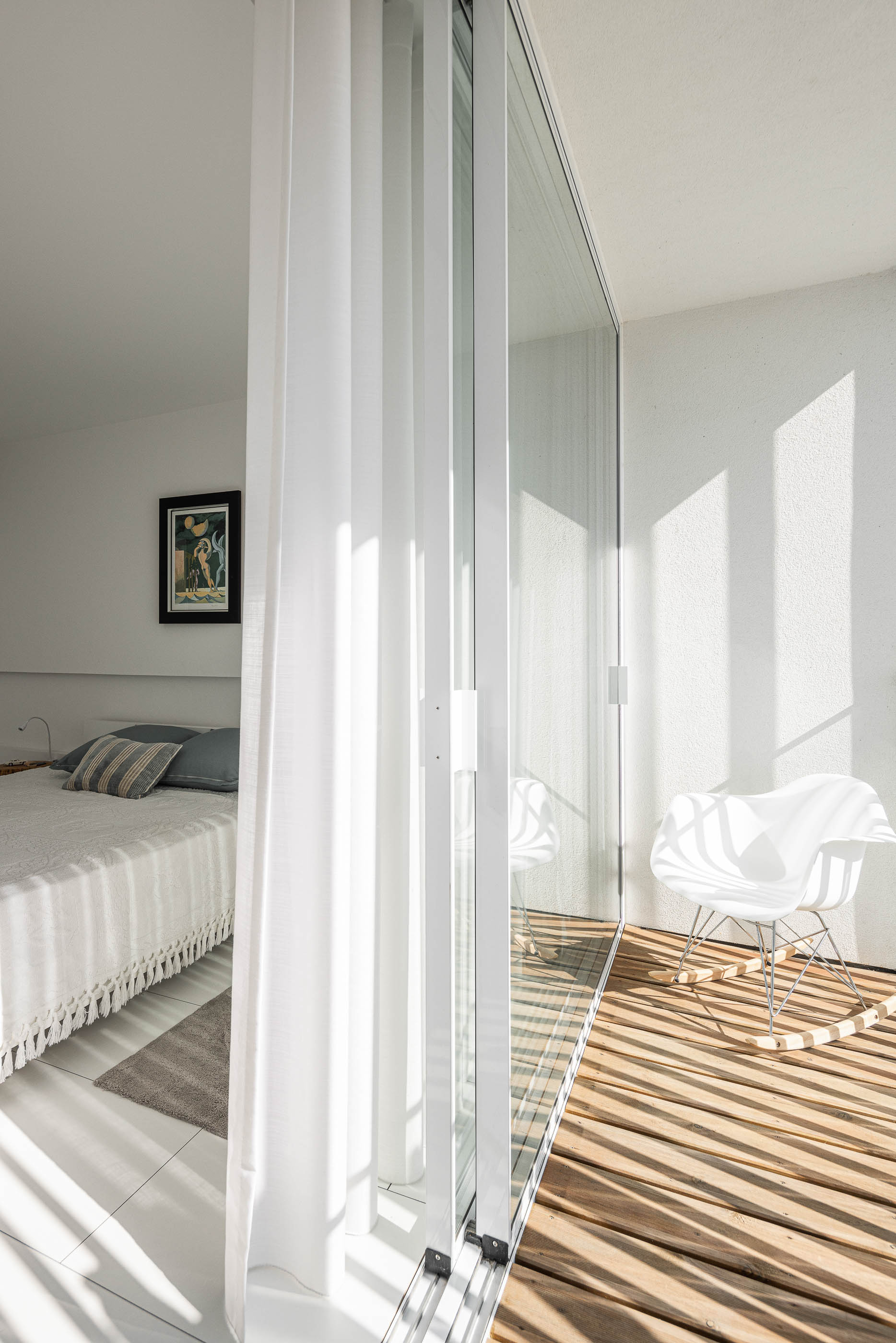 Quarto: Cama com roupa branca e almofadas cinzentas, alcatifa geométrica e acesso à varanda com cadeira e pavimento de madeira. — Casa Cor de Sal arquitetura Rómulo Neto Arquitectos em Ílhavo