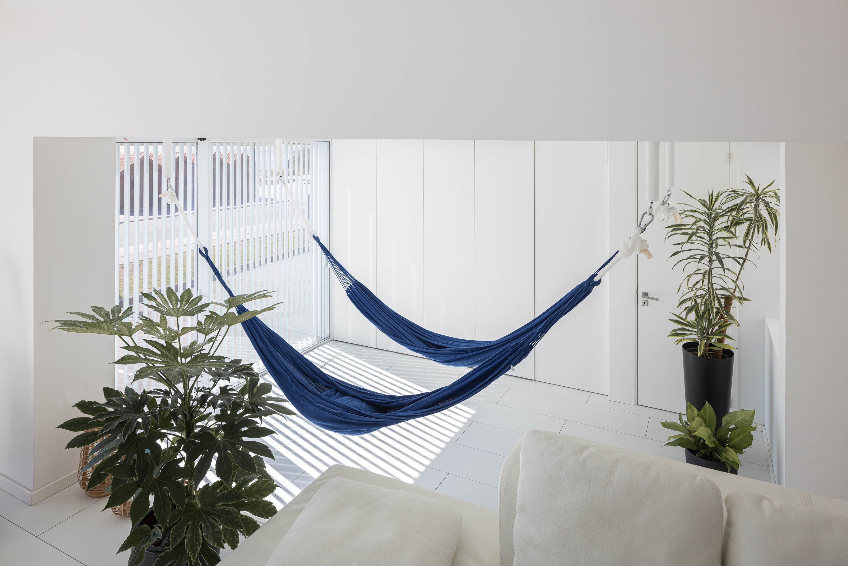 Mezzanine: Vista superior da rede azul suspensa, com armários brancos embutidos e plantas decorativas. — Casa Cor de Sal arquitetura Rómulo Neto Arquitectos em Ílhavo
