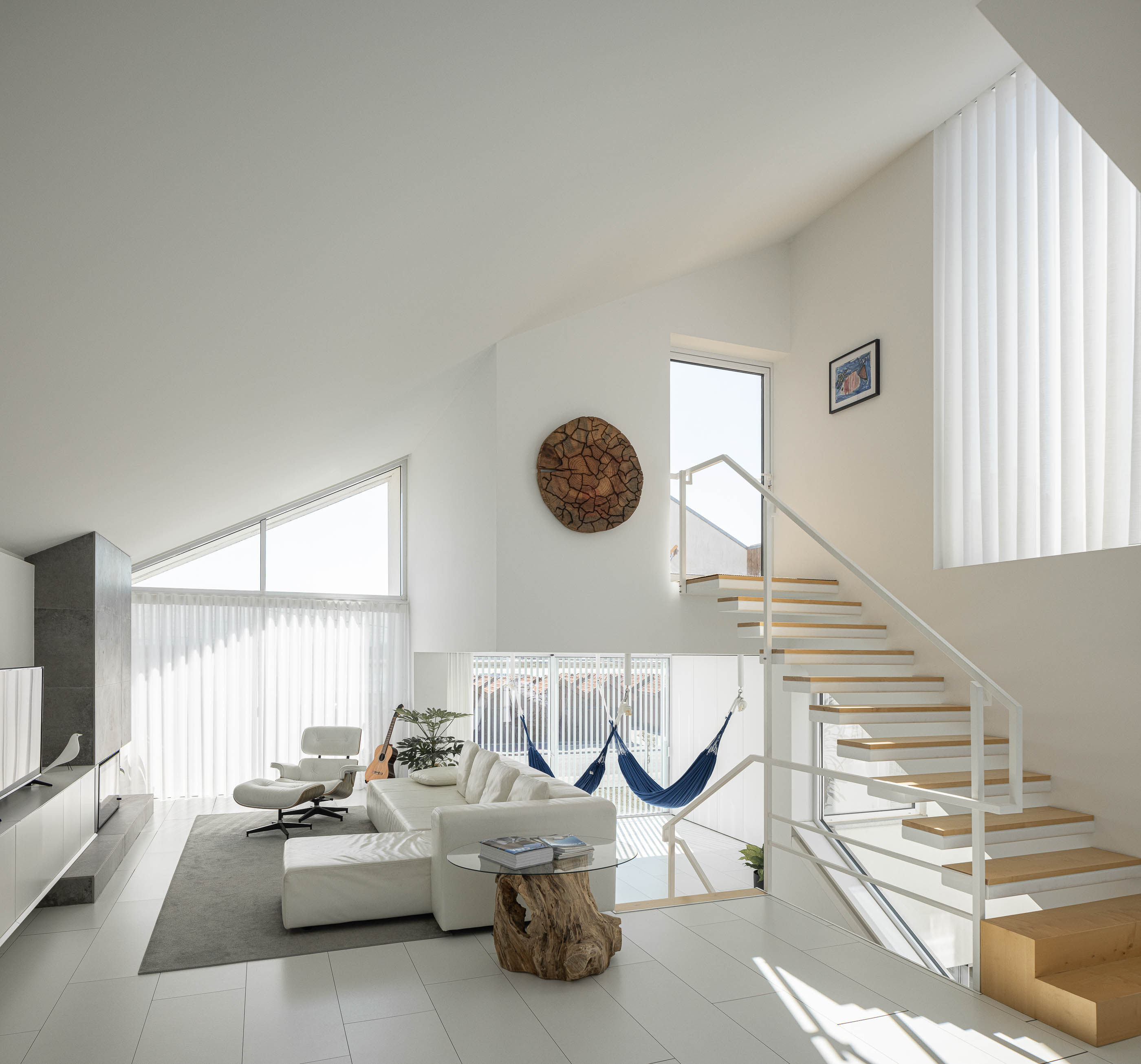 Sala de estar: Escadaria branca e madeira, sofá branco, lareira em pedra cinzenta e rede azul suspensa. — Casa Cor de Sal arquitetura Rómulo Neto Arquitectos em Ílhavo