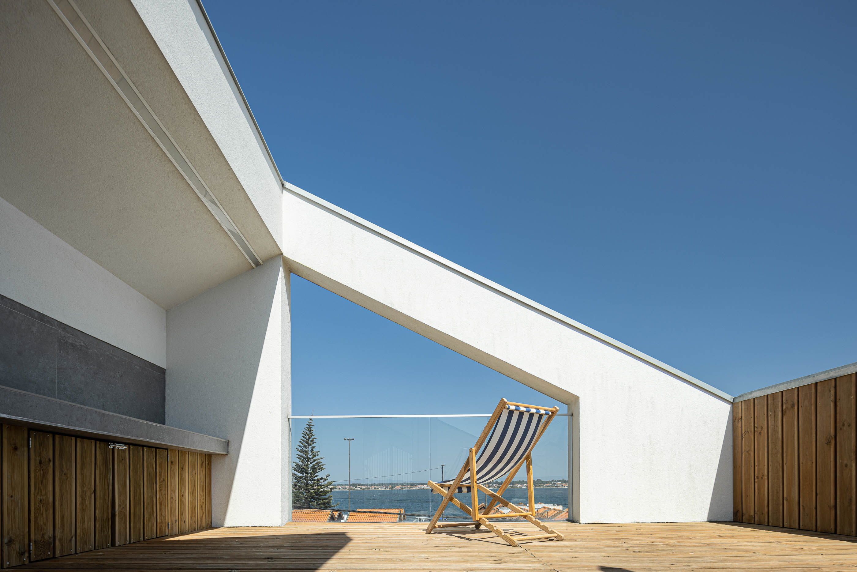 Terraço: Espaço exterior com churrasqueira, pavimento de madeira e vista para a paisagem marítima. — Casa Cor de Sal arquitetura Rómulo Neto Arquitectos em Ílhavo