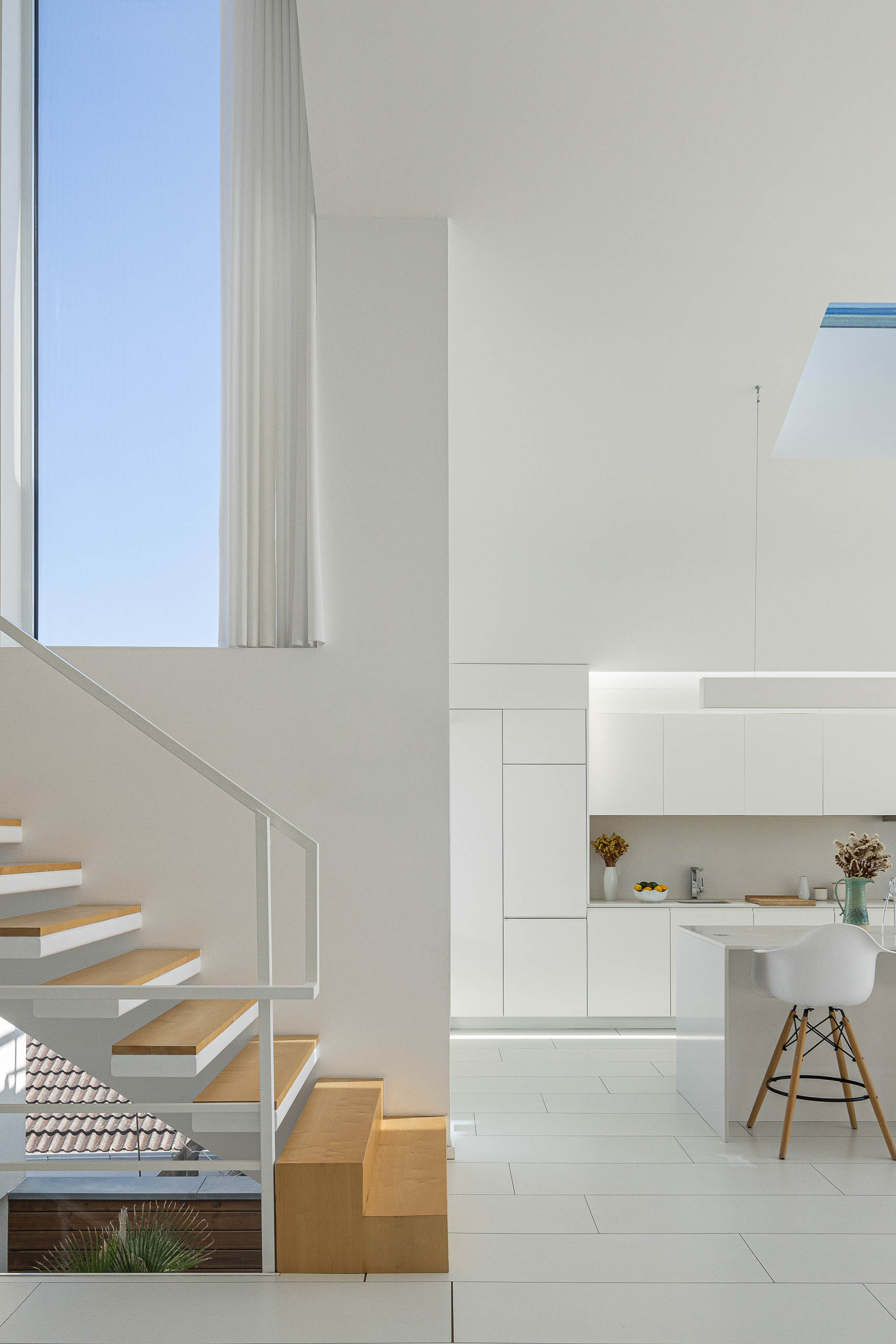 Cozinha: Espaço amplo com armários brancos, ilha central e escadaria de madeira e branca. — Casa Cor de Sal arquitetura Rómulo Neto Arquitectos em Ílhavo