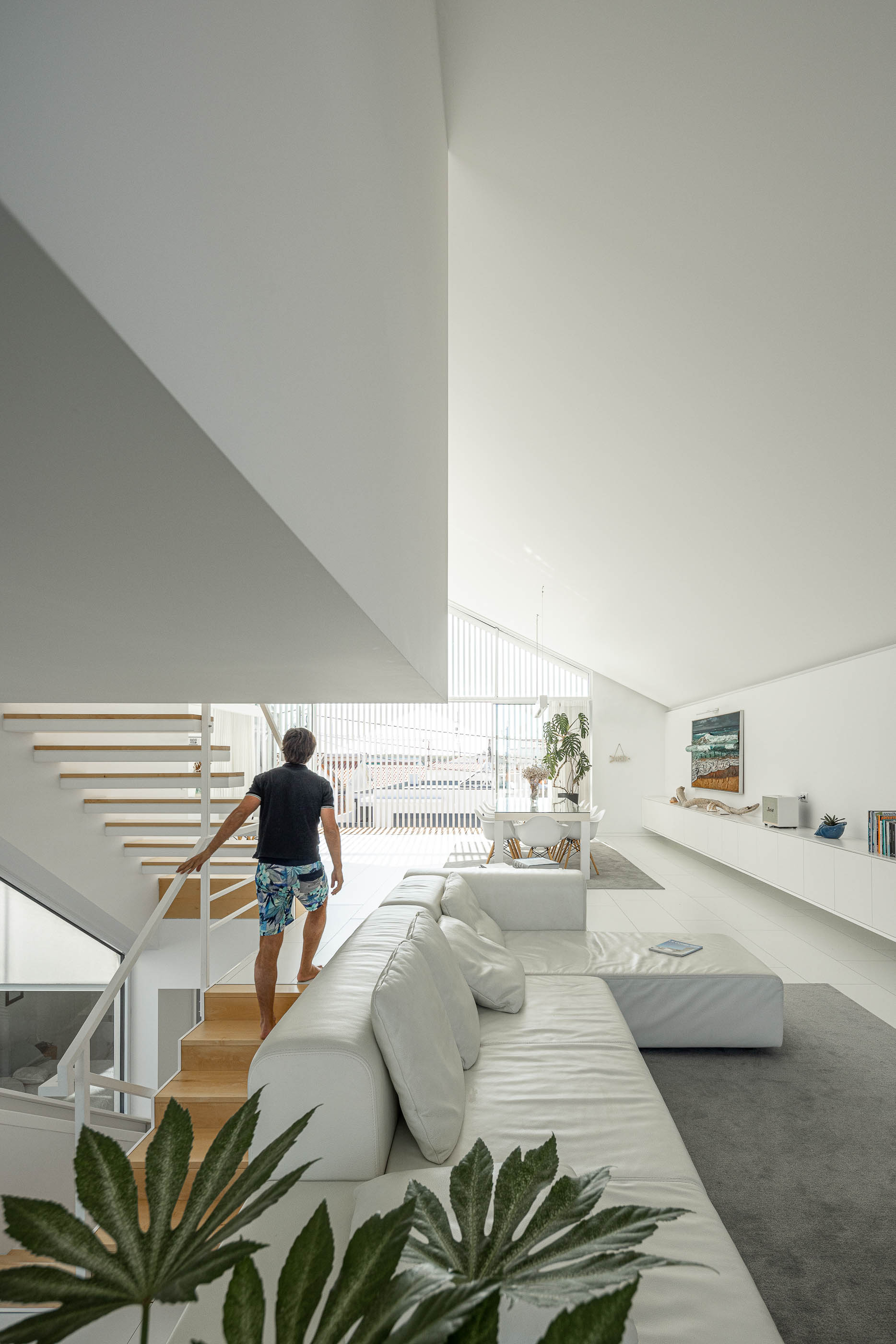 Sala de estar: Escadaria de madeira, sofá branco e vista para a sala de jantar e cozinha. — Casa Cor de Sal arquitetura Rómulo Neto Arquitectos em Ílhavo