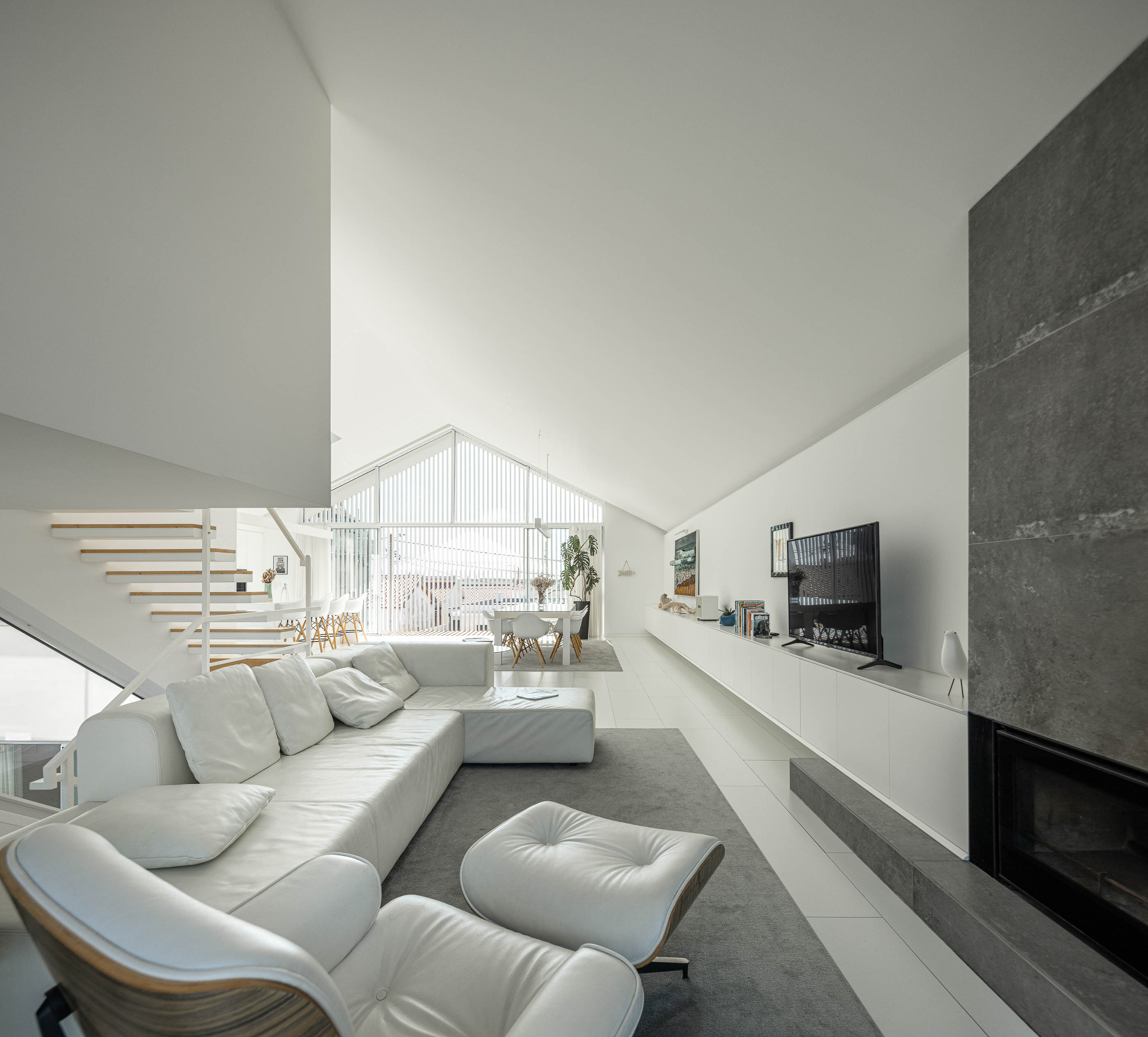 Sala de estar: Sofá branco, lareira em pedra cinzenta, escadaria de madeira e sala de jantar ao fundo. — Casa Cor de Sal arquitetura Rómulo Neto Arquitectos em Ílhavo