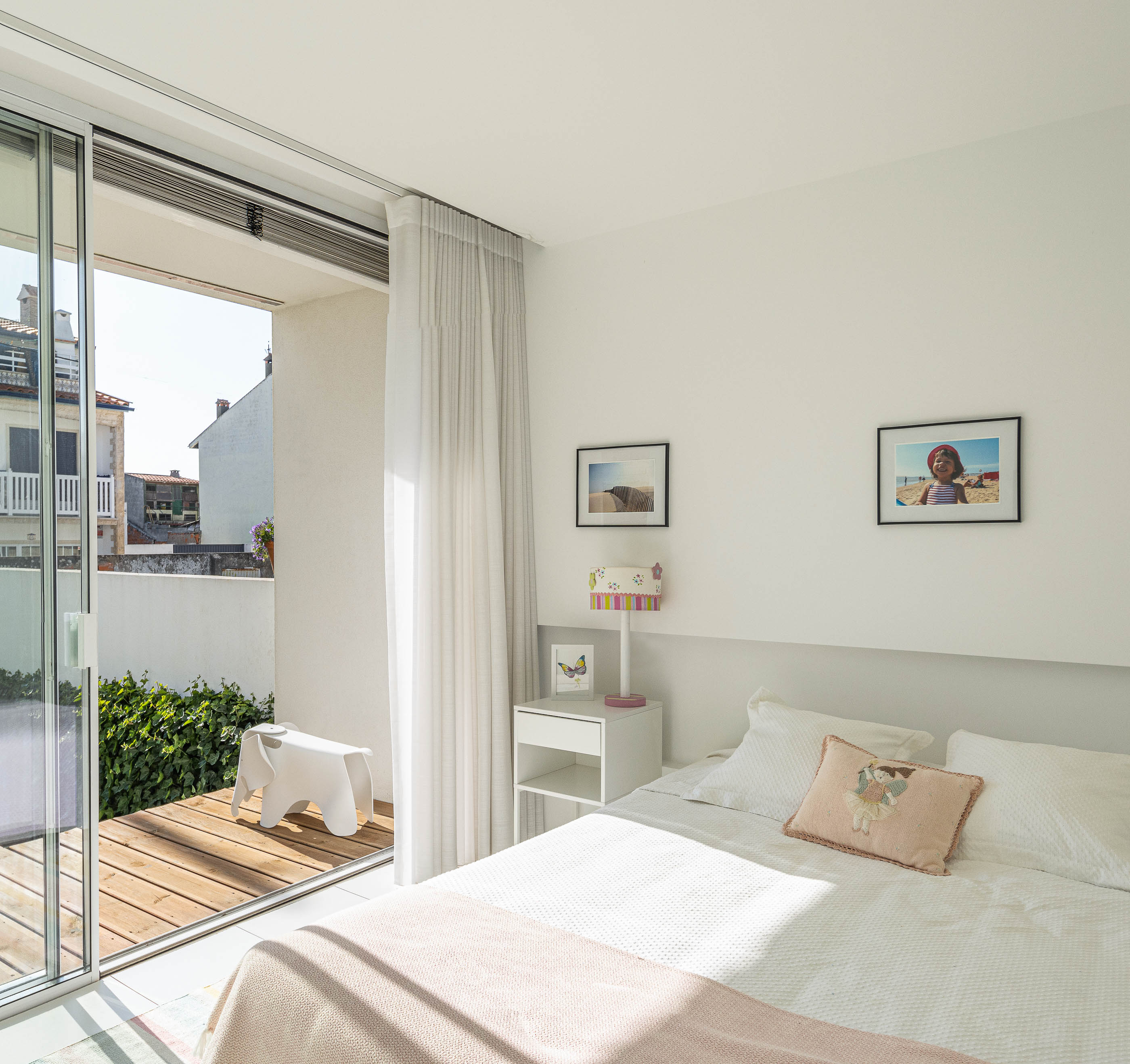 Quarto: Cama com roupa de cama branca, fotografias na parede e acesso à varanda com pavimento de madeira. — Casa Cor de Sal arquitetura Rómulo Neto Arquitectos em Ílhavo