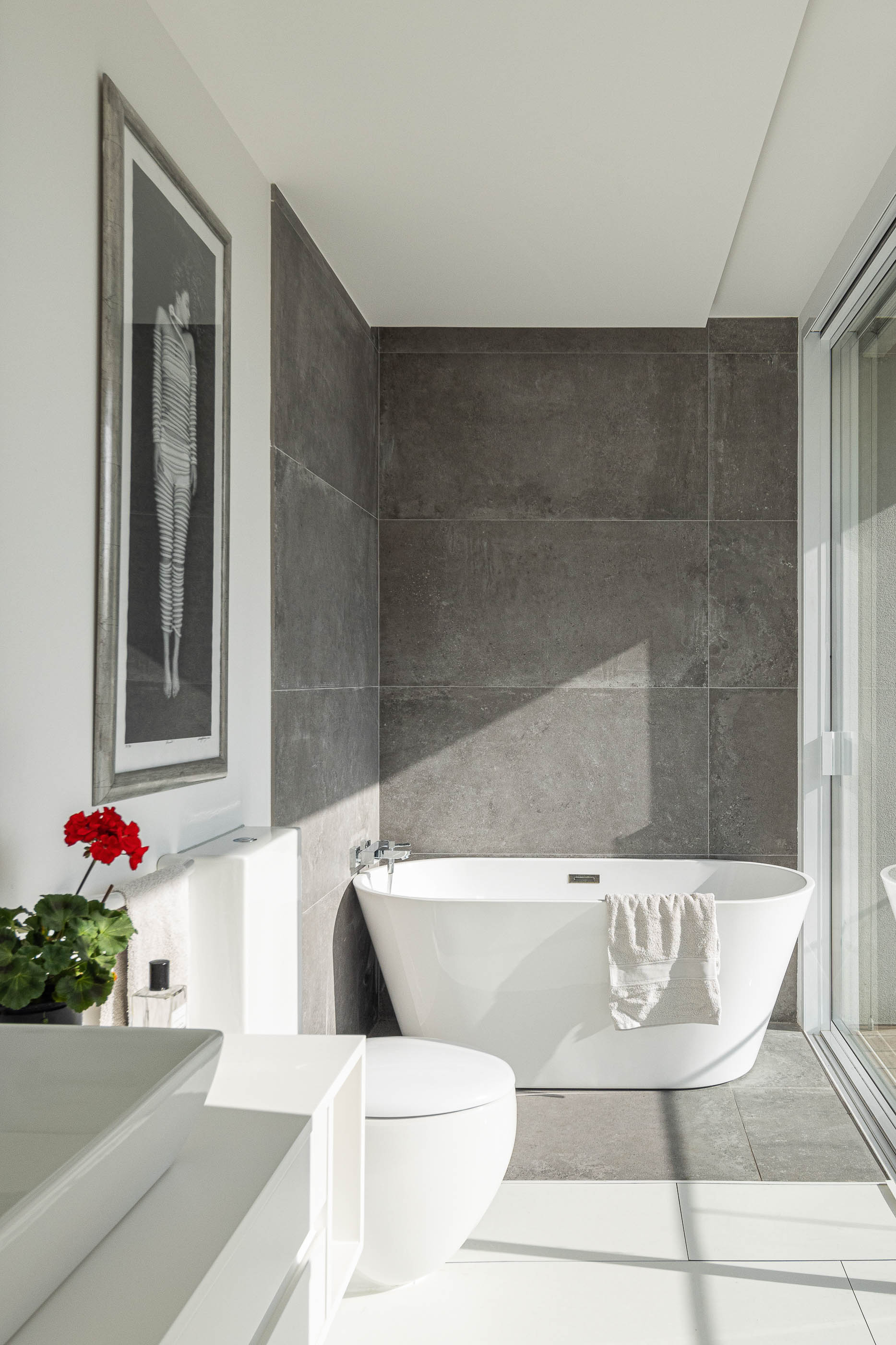 Casa de banho: Banheira branca, sanita suspensa e revestimento cinzento nas paredes. — Casa Cor de Sal arquitetura Rómulo Neto Arquitectos em Ílhavo
