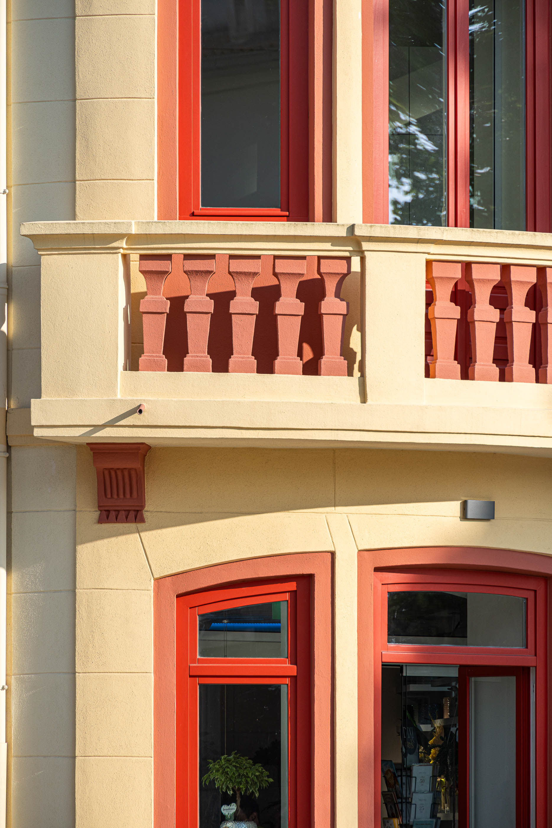 Fachada: Pormenor da varanda com balaustrada, caixilharia vermelha e detalhes decorativos na fachada creme. — A'mar arquitetura REM'A Arquitectos em Póvoa de Varzim