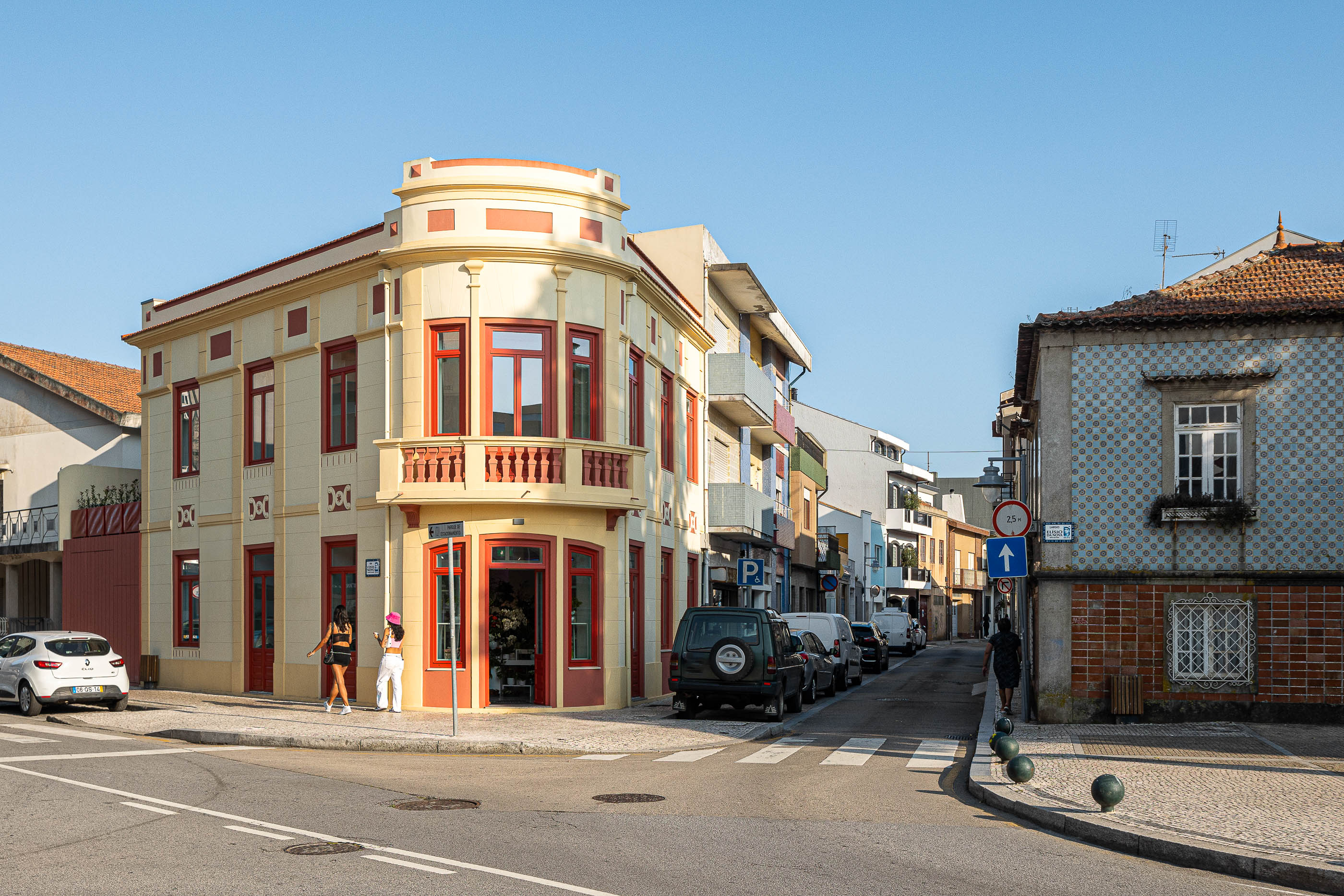 Fachada: Edifício de esquina com varanda curva, em tons creme e vermelho, numa rua da Póvoa de Varzim. — A'mar arquitetura REM'A Arquitectos em Póvoa de Varzim