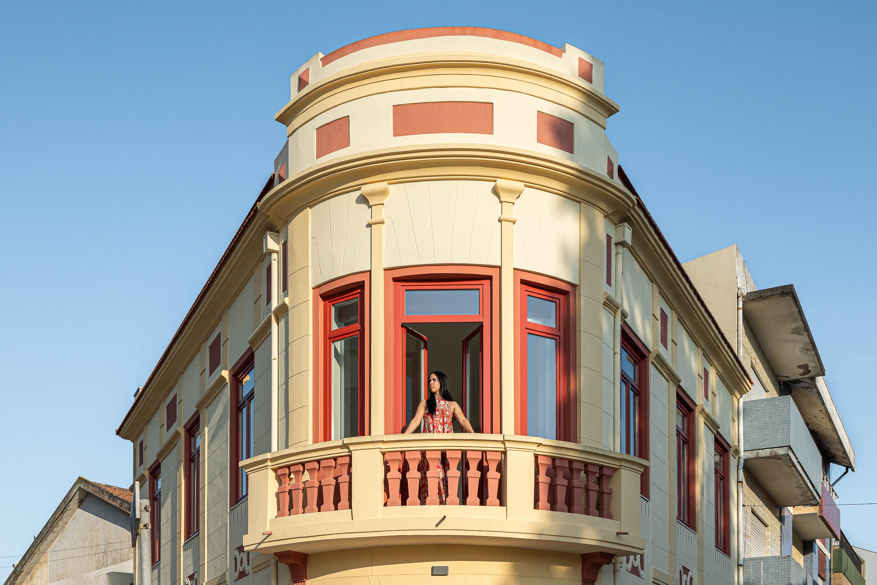 Fachada: Vista de cima da varanda curva do edifício, com caixilharia vermelha e detalhes clássicos. — A'mar arquitetura REM'A Arquitectos em Póvoa de Varzim