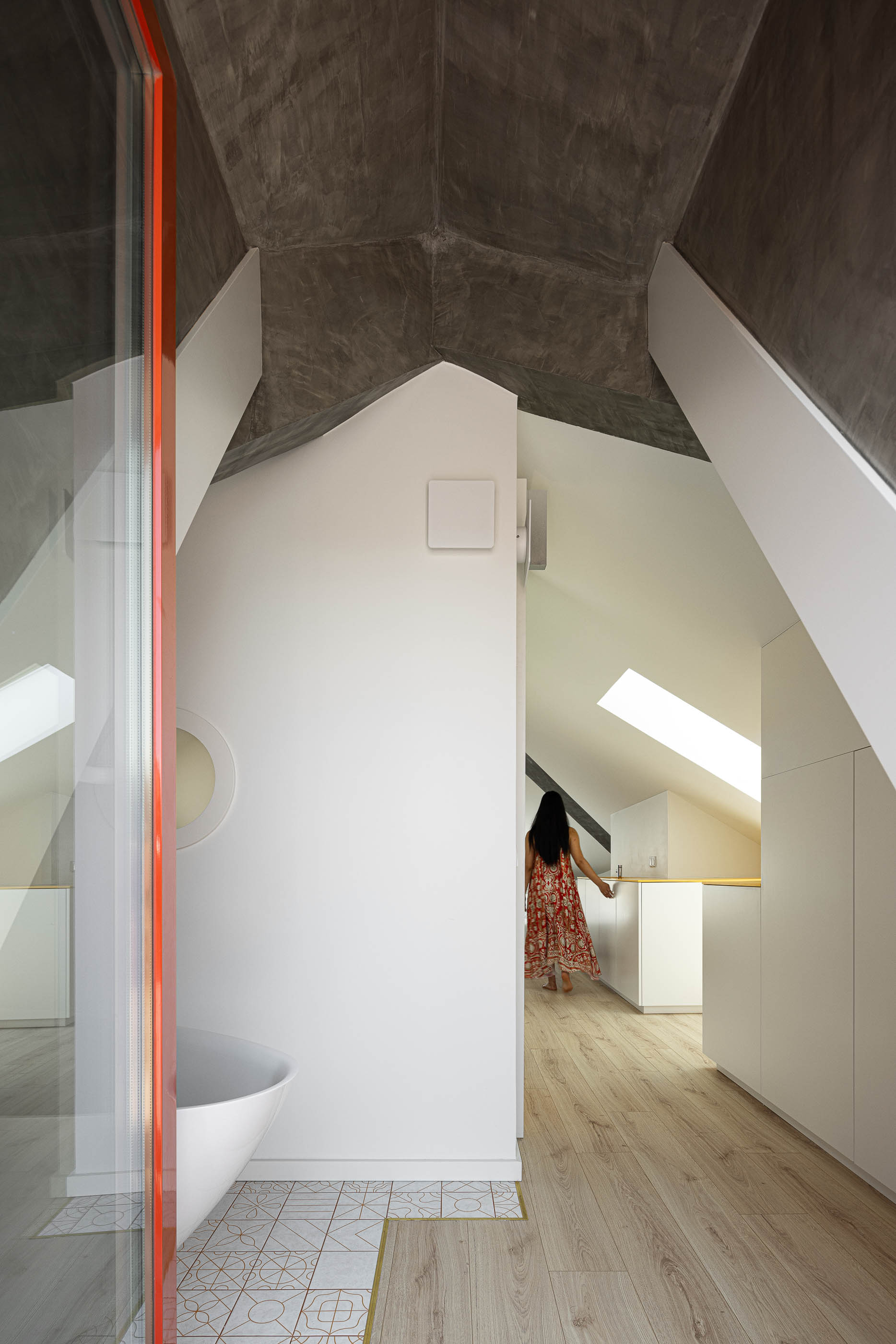 Casa de banho: Interior com banheira branca, pavimento cerâmico decorado e teto inclinado em betão. — A'mar arquitetura REM'A Arquitectos em Póvoa de Varzim